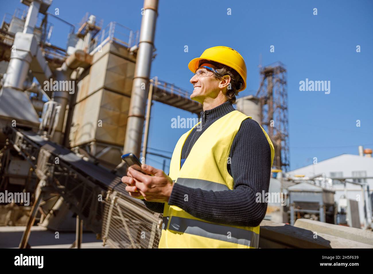 Cheerful man engineer using smartphone at industrial site Stock Photo