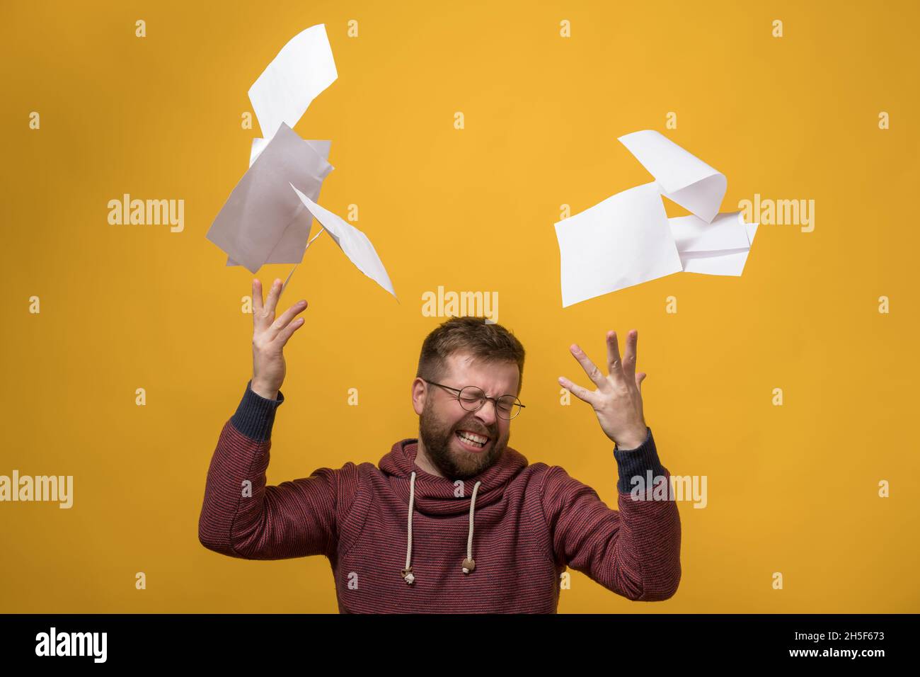 Man is stressed, he throwing a stack of white paper up, squeezes eyes shut and clenching her teeth. Bad working day. Copy space.  Stock Photo