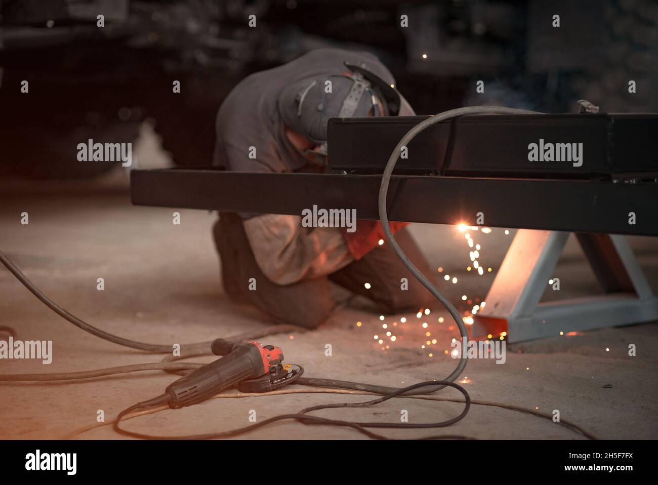 A welder in a car will weld a truck frame. Near the worker lies the grinder tool. Focus