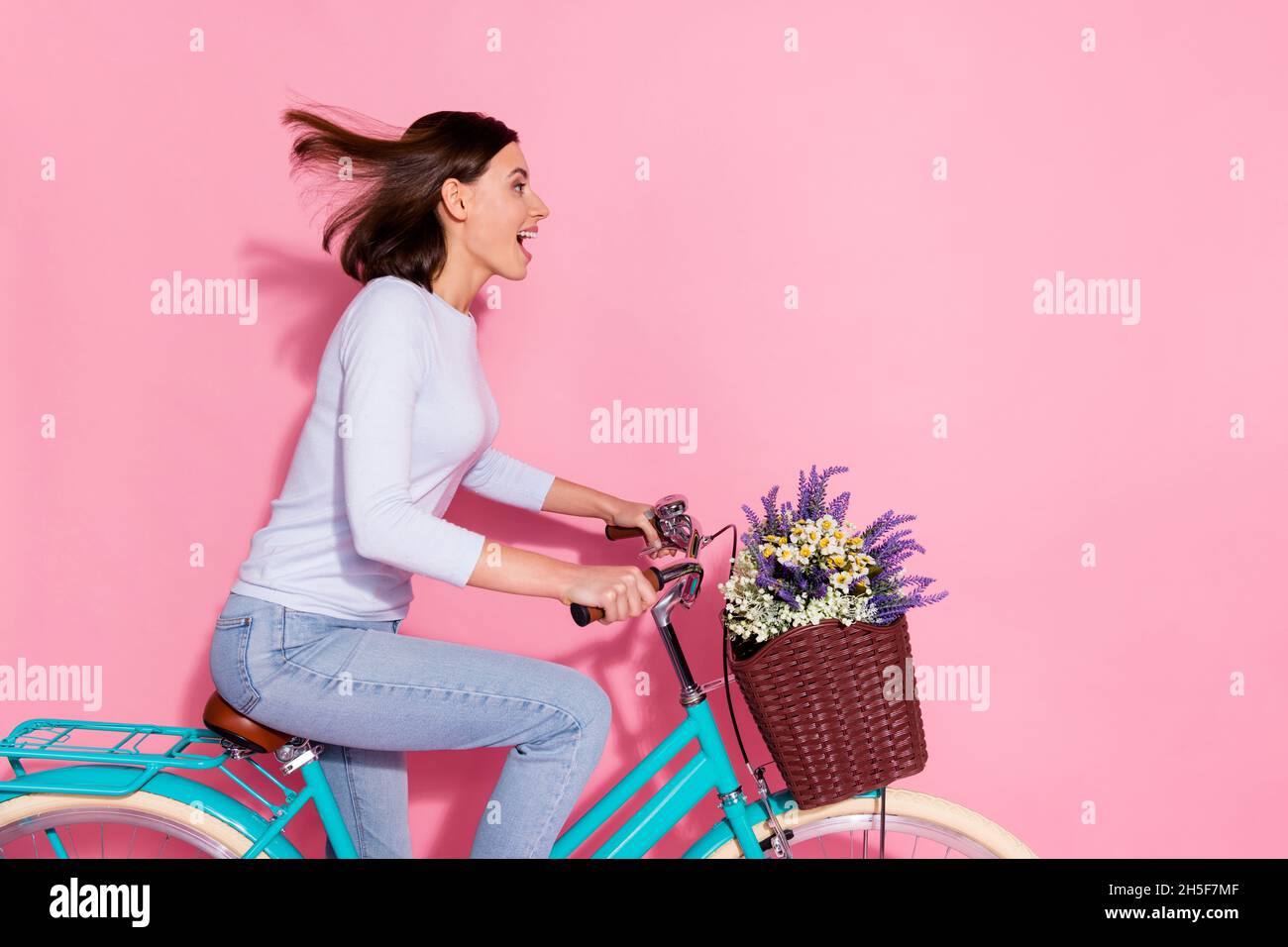 Photo of funny excited young lady dressed white jumper smiling riding bicycle looking empty space isolated pink color background Stock Photo