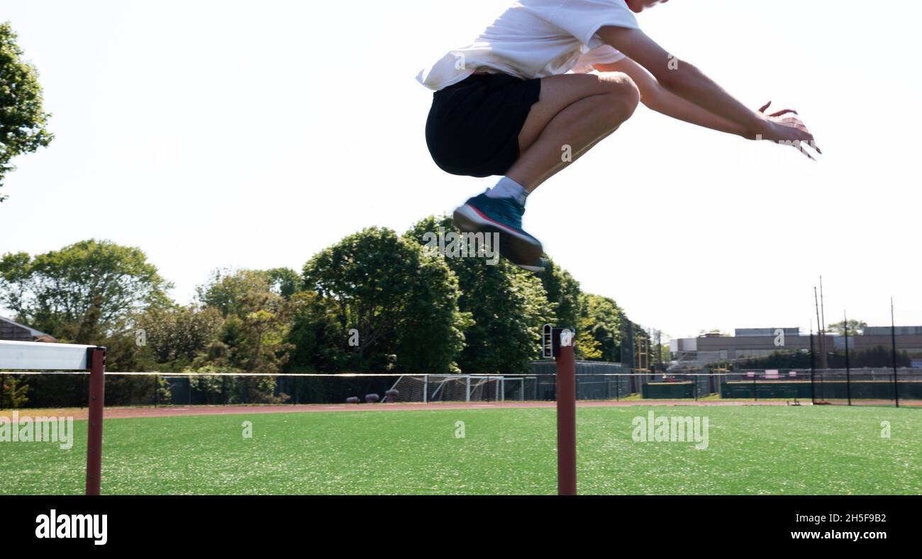 A high school athlete is jumping over track hurdles placed on a turf field at track and field practice. Stock Photo