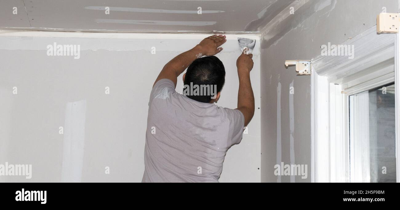 A contractor taping and spackling drywall sheetrock inside a residential home. Stock Photo