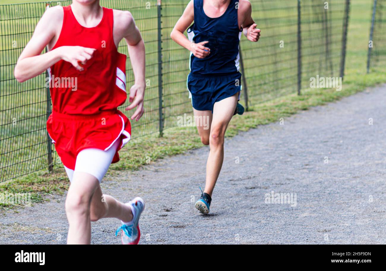 Two high school boys finishing a cross country running race on a gravel path next to a fence at Van Cortlandt park in the Bronx New York. Stock Photo