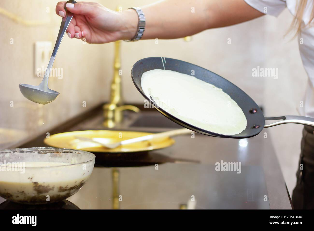 A woman prepares Russian pancakes in the kitchen, a close-up on a frying pan. the concept of Russian cuisine, cookery, Maslenitsa holiday. Homemade he Stock Photo