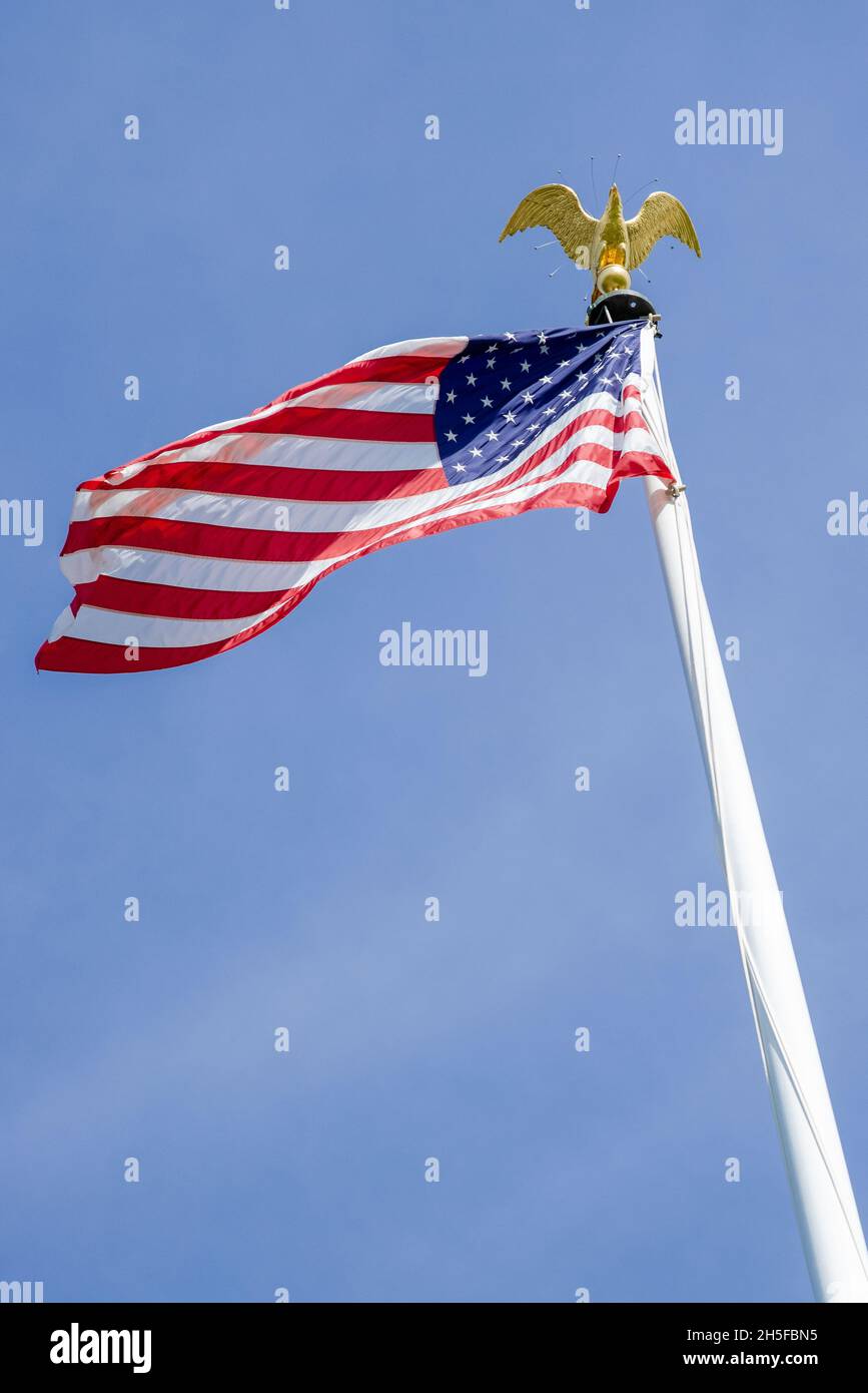 American flag waving in the wind against a blue sky with an eagle on the pole at the ABMC cemetery in Luxemburg, Europe. Stock Photo