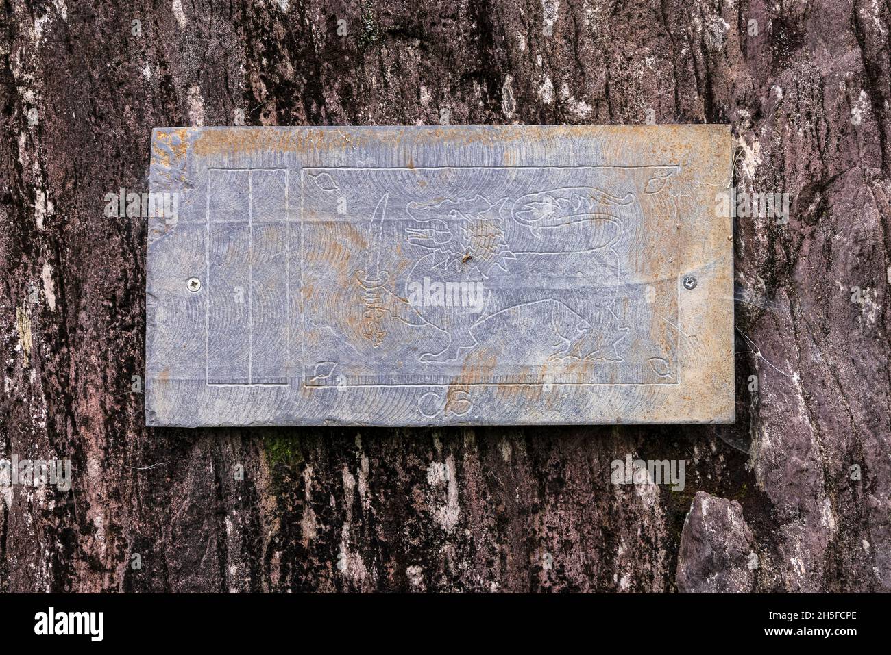 Slate plaque with carved dragon holding a sword fixed to a rock in the Glengarriff Woods Nature Reserve, Glengarriff, County Cork, Ireland Stock Photo