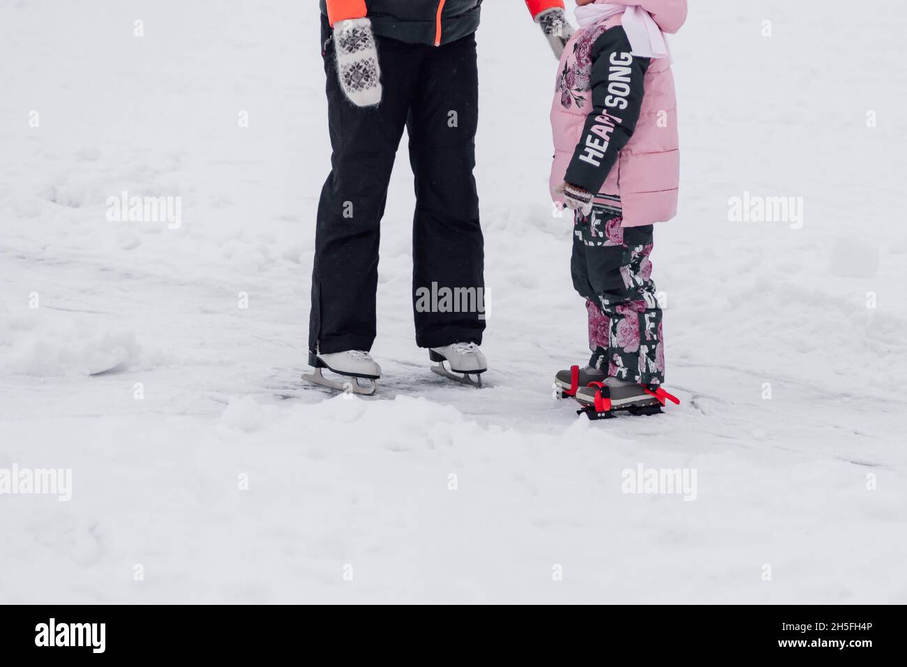 Close-up of human legs and figure skating skates. Young woman and little girl skate on ice in winter in nature Stock Photo