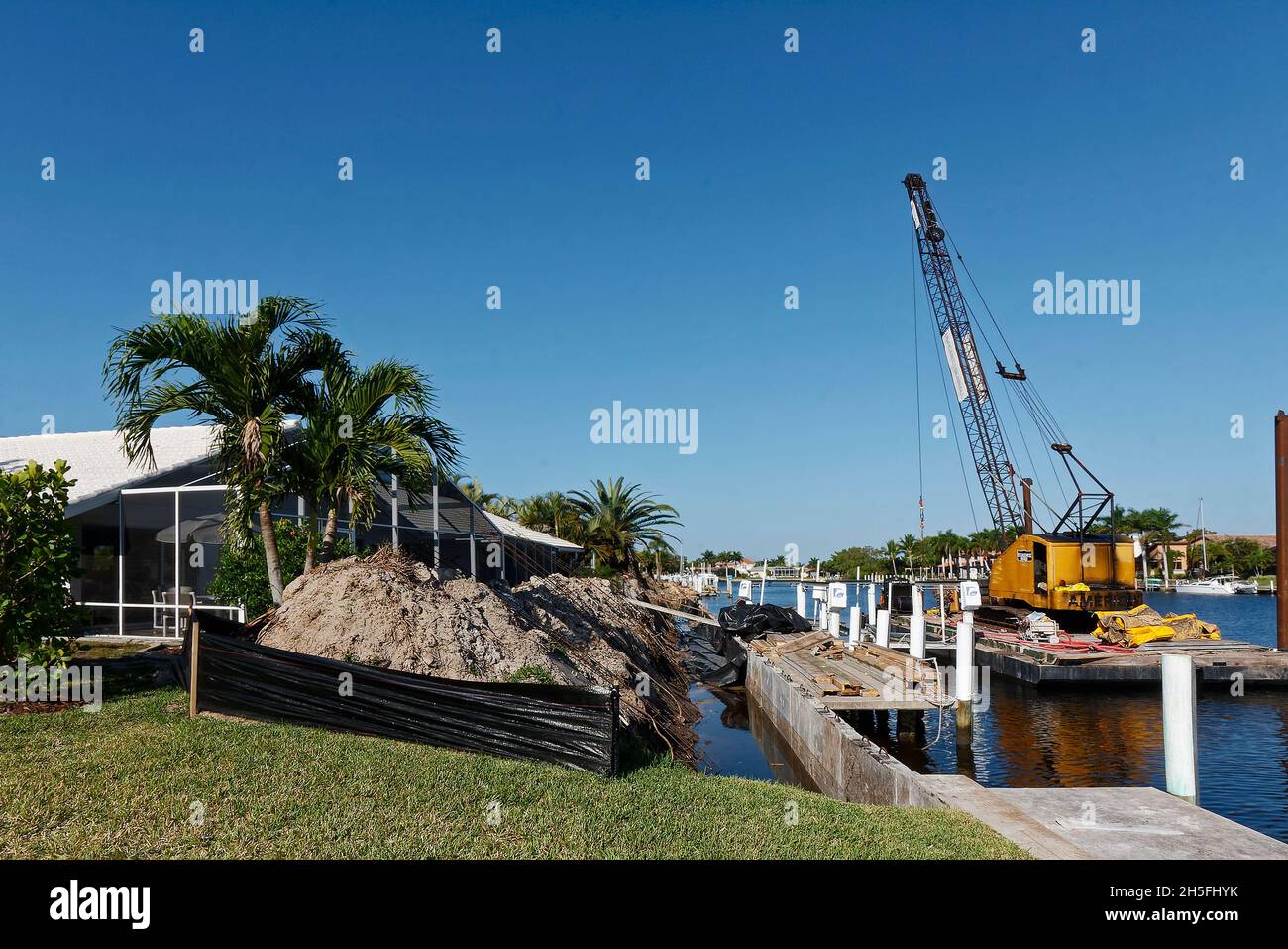 repairing seawall, crane on barge, heavy equipment, maintenance, dirt piles, docks, houses