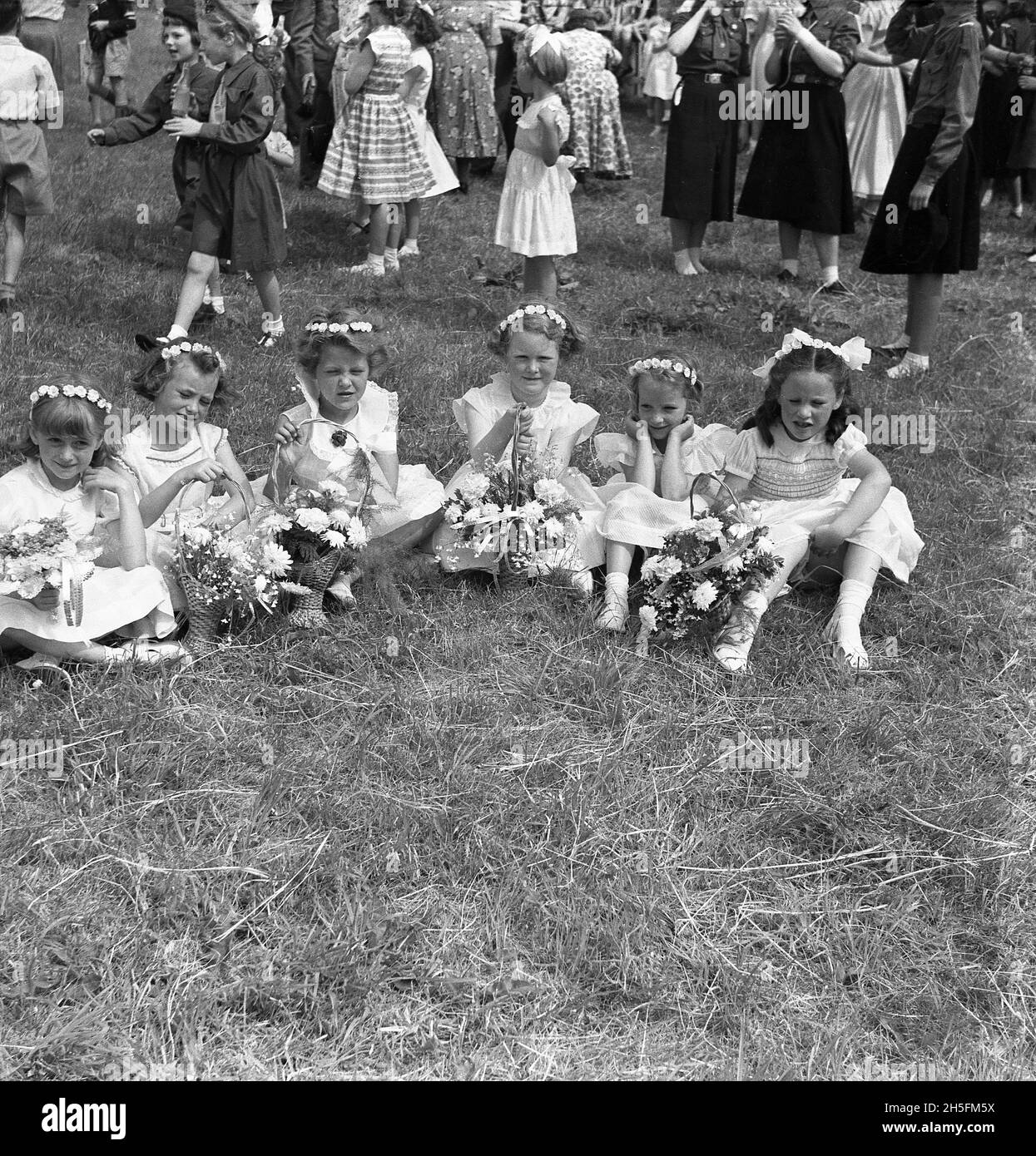 1950s, historical, young girls in their sunday school outfits and with flower bouquets, sitting down on the grass at a local park, having taken part in a street procession with their families for the Audley Range Congregational Church, Audley Range, Blackburn, Lancashire, England, UK. From the 1840s, the industrial revolution and the growth of the cotton and textile industries had transformed the area and terraced housing, schools, shops, pubs and churches were built on farm land to service the new population working in the factories and textile mills. Stock Photo
