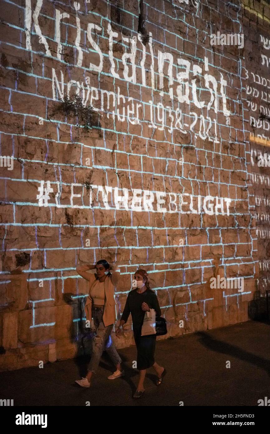 Jerusalem, Israel. 9th Nov, 2021. People walk past projections on the Old City walls near the Jaffa Gate as the International March of the Living commemorates Kristallnacht around the world. The global campaign of unity, Let There Be Light, encourages solidarity against antisemitism, racism, hatred and intolerance on the night of November 9th. Kristallnacht, the Night of Broken Glass, 9th November 1938, saw the destruction of thousands of synagogues, Jewish institutions and Jewish owned businesses in Germany. Credit: Nir Alon/Alamy Live News Stock Photo