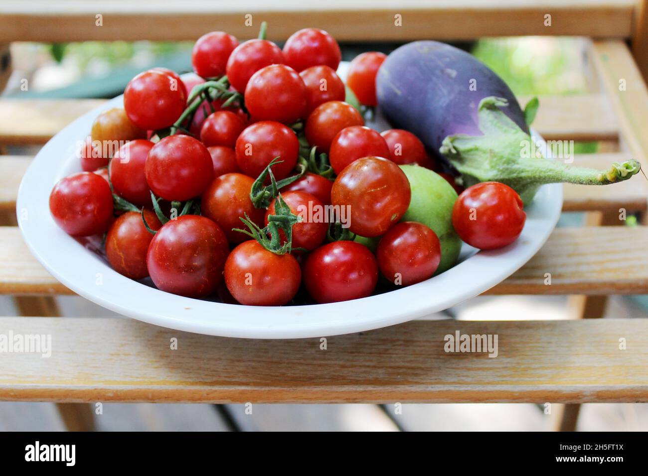 Ein Teller mit Gemüse (Kirschtomaten und Aubergine) auf einem Holzstuhl, Kroatien. Stock Photo