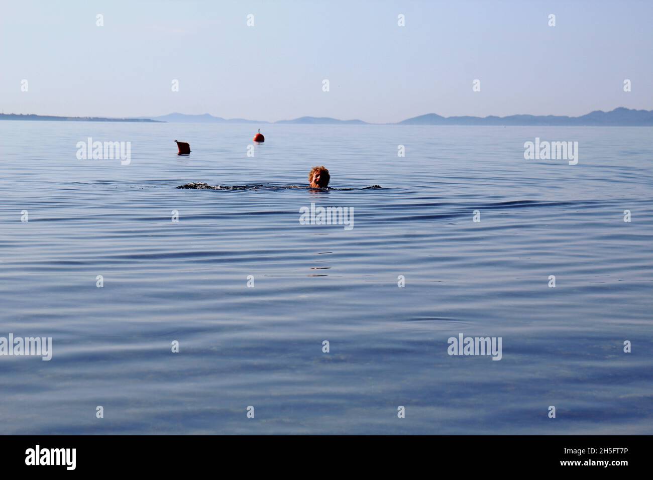 Mann schwimmt im Meer: Kopf eines Mannes, der aus dem Wasser ragt. Sein Gesicht ist schmerzverzerrt / schreiend. Bojen im Hintergrund. Vir, Kroatien. Stock Photo