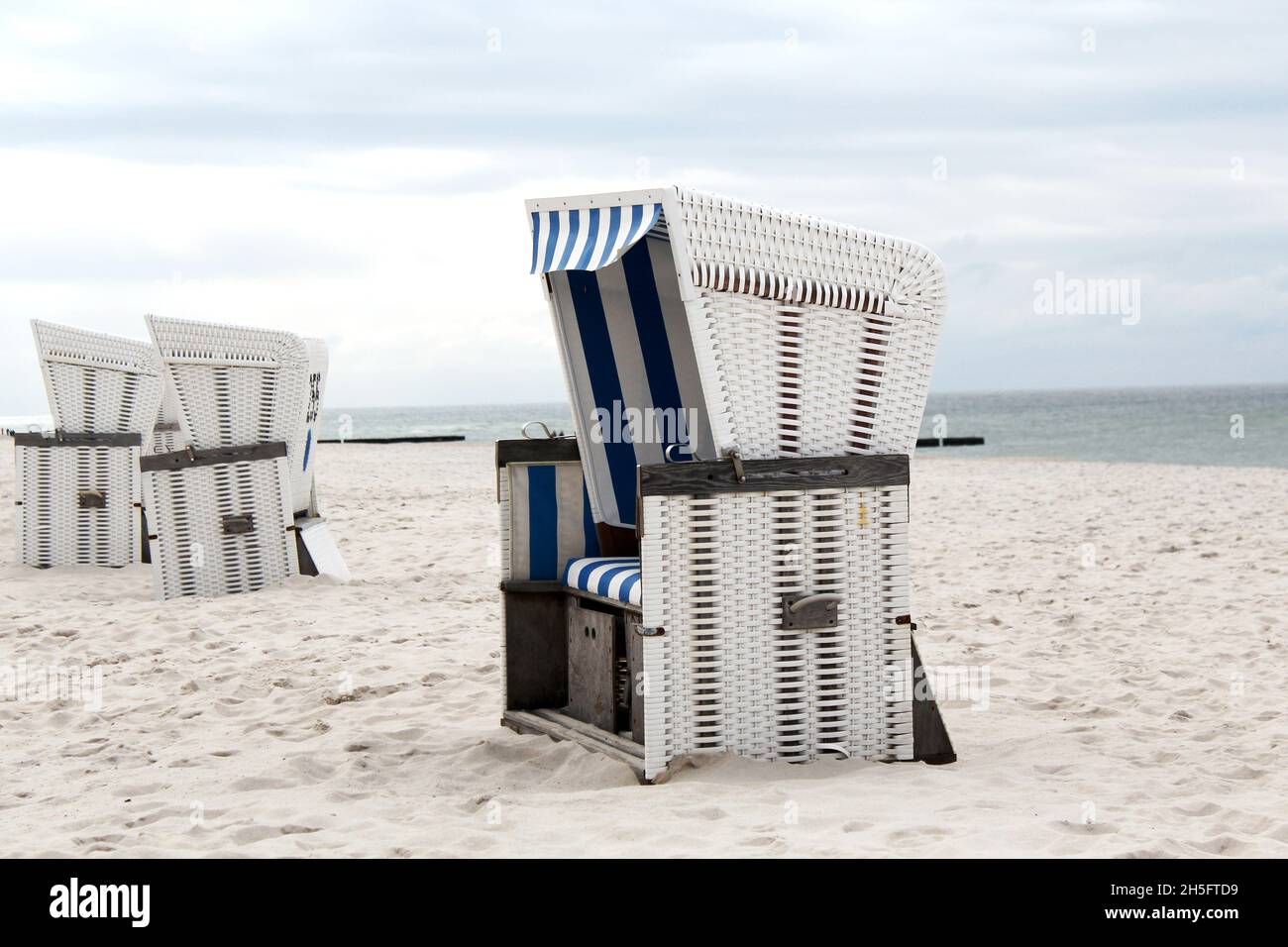 Mehrere weiße, geflochtene Strandkörbe mit blau weißen Streifen am leeren Strand von Sylt, Deutschland. Stock Photo