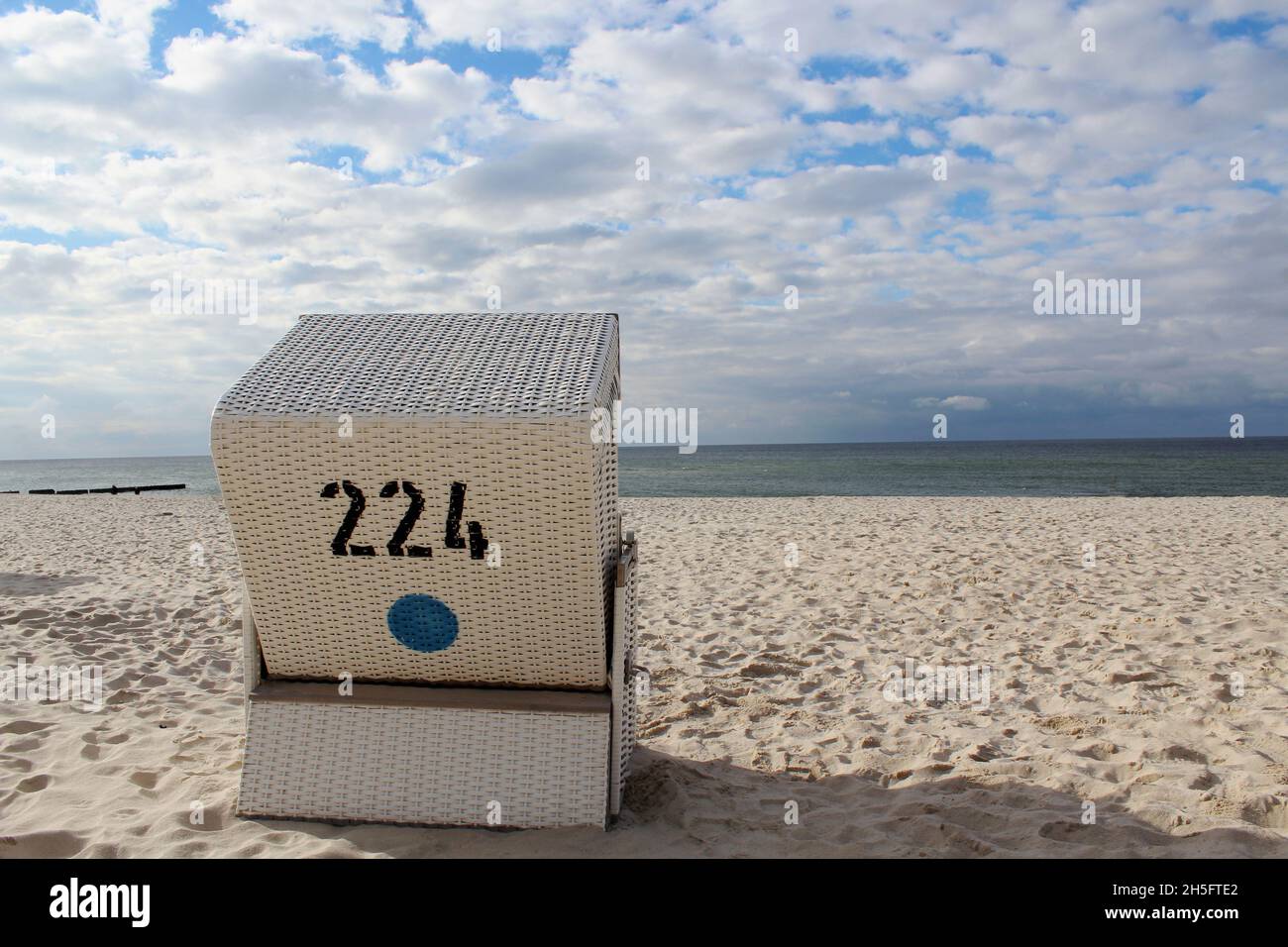 Ein weißer, geflochtener Strandkorb von hinten mit Blick auf das Wasser am leeren Strand von Sylt, Deutschland. Stock Photo