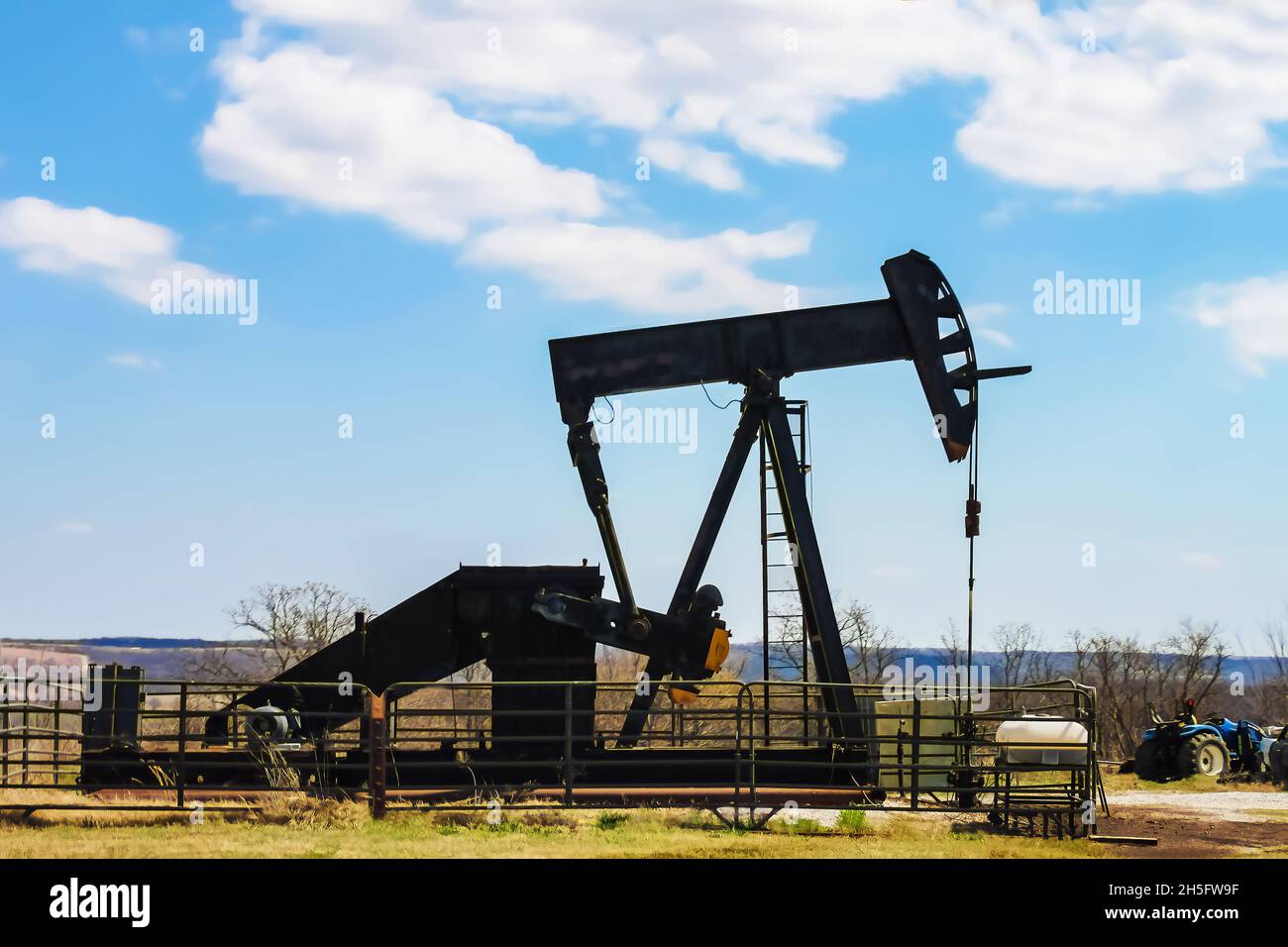 Oil well pump jack silhouette in metal cattle fence with blue hills in