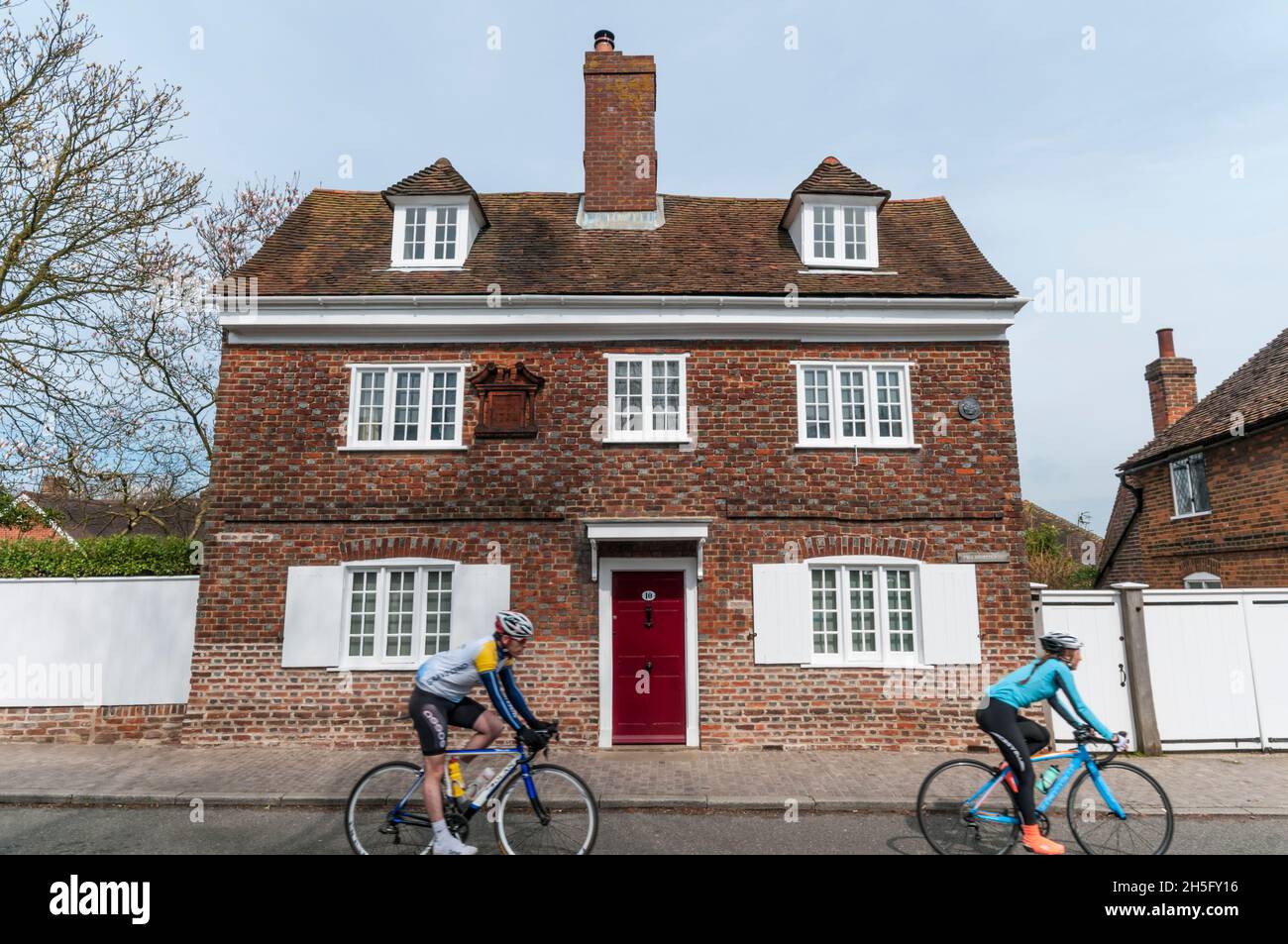 Two cyclists (motion blurred} passing 17th century Mill Farmhouse in The Street, Cobham, Kent. Stock Photo