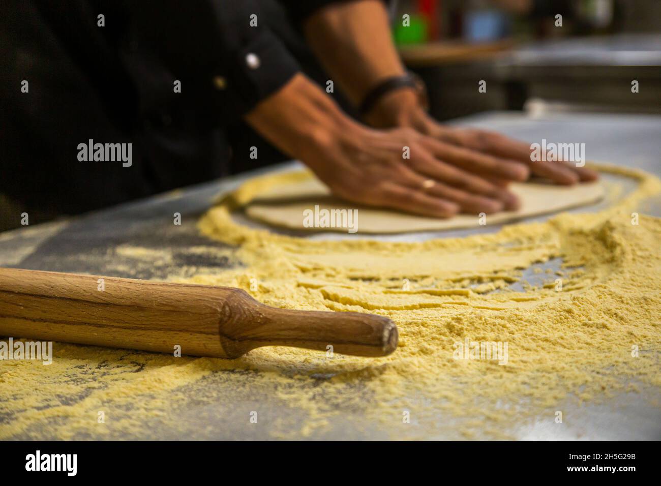 Professional chef cooking in the kitchen restaurant at the hotel, preparing dinner. A cook in an apron makes a pizza. man rolls out pizza dough Stock Photo