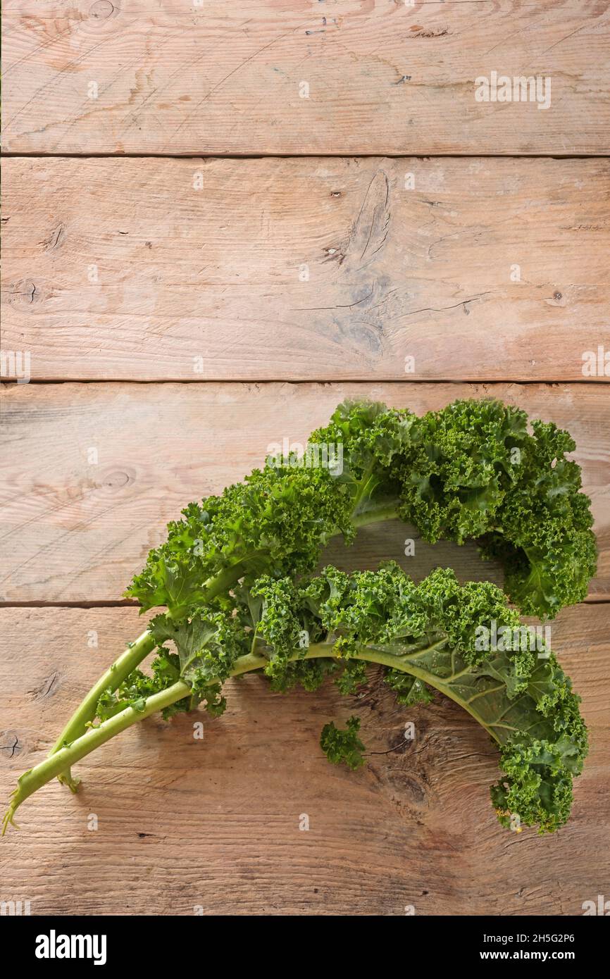 Curly leaves of kale or green leaf cabbage on rustic wooden planks, vertical format with large copy space for an announcement poster, copy space, top Stock Photo
