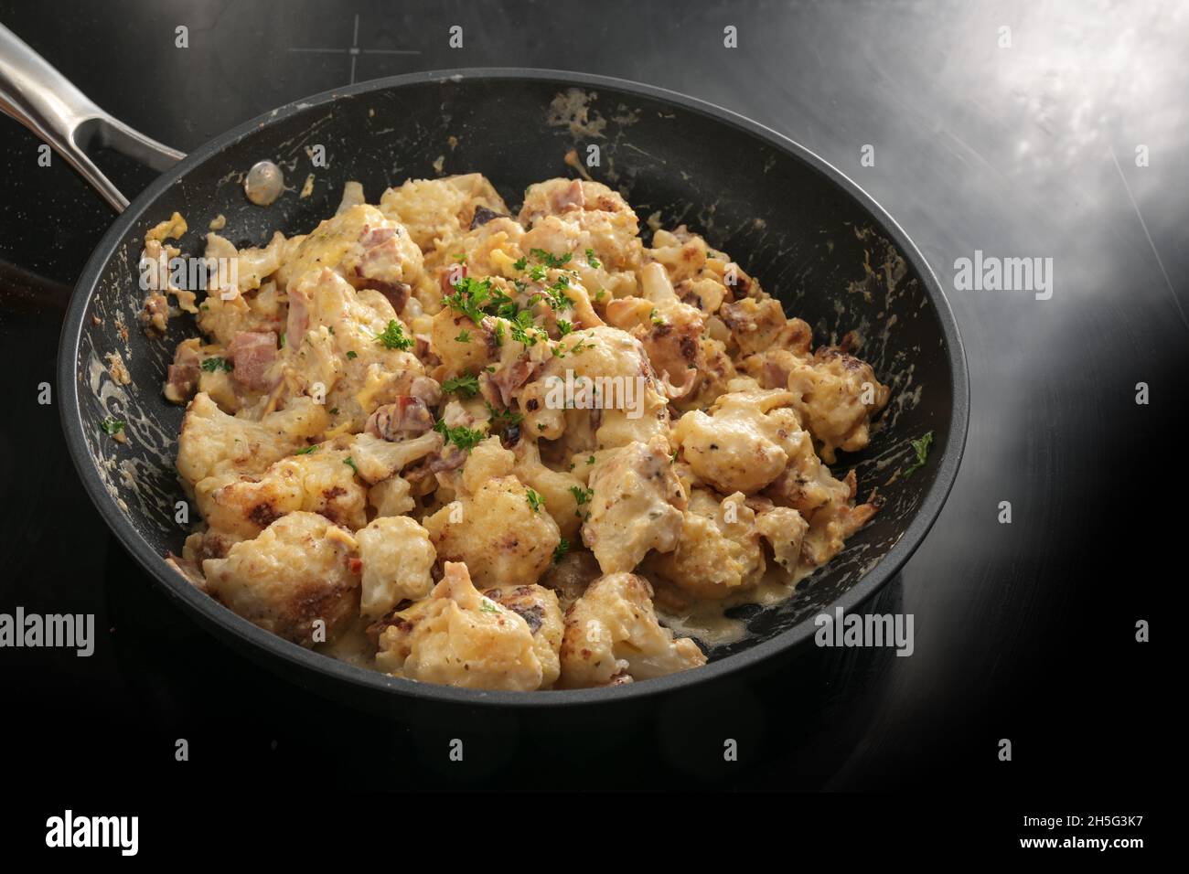 Frying pan with cauliflower florets, ham and a sauce from cream, cheese and egg, parsley garnish, cooking with vegetables for a ketogenic or low carb Stock Photo
