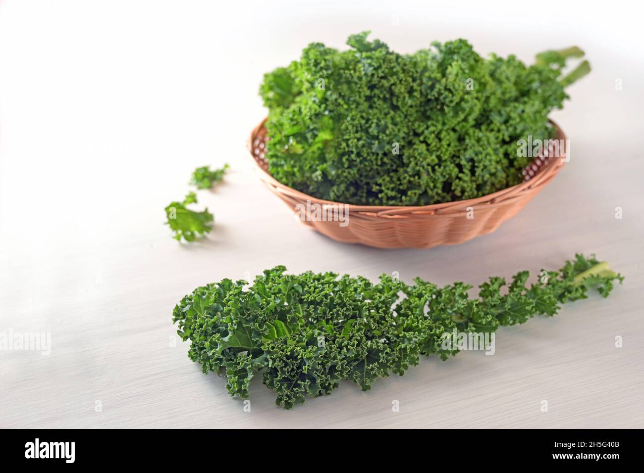 Kale or green leaf cabbage, one curly leaf and more collected in a basket on a white table, winter vegetable rich in vitamins, copy space, selected fo Stock Photo