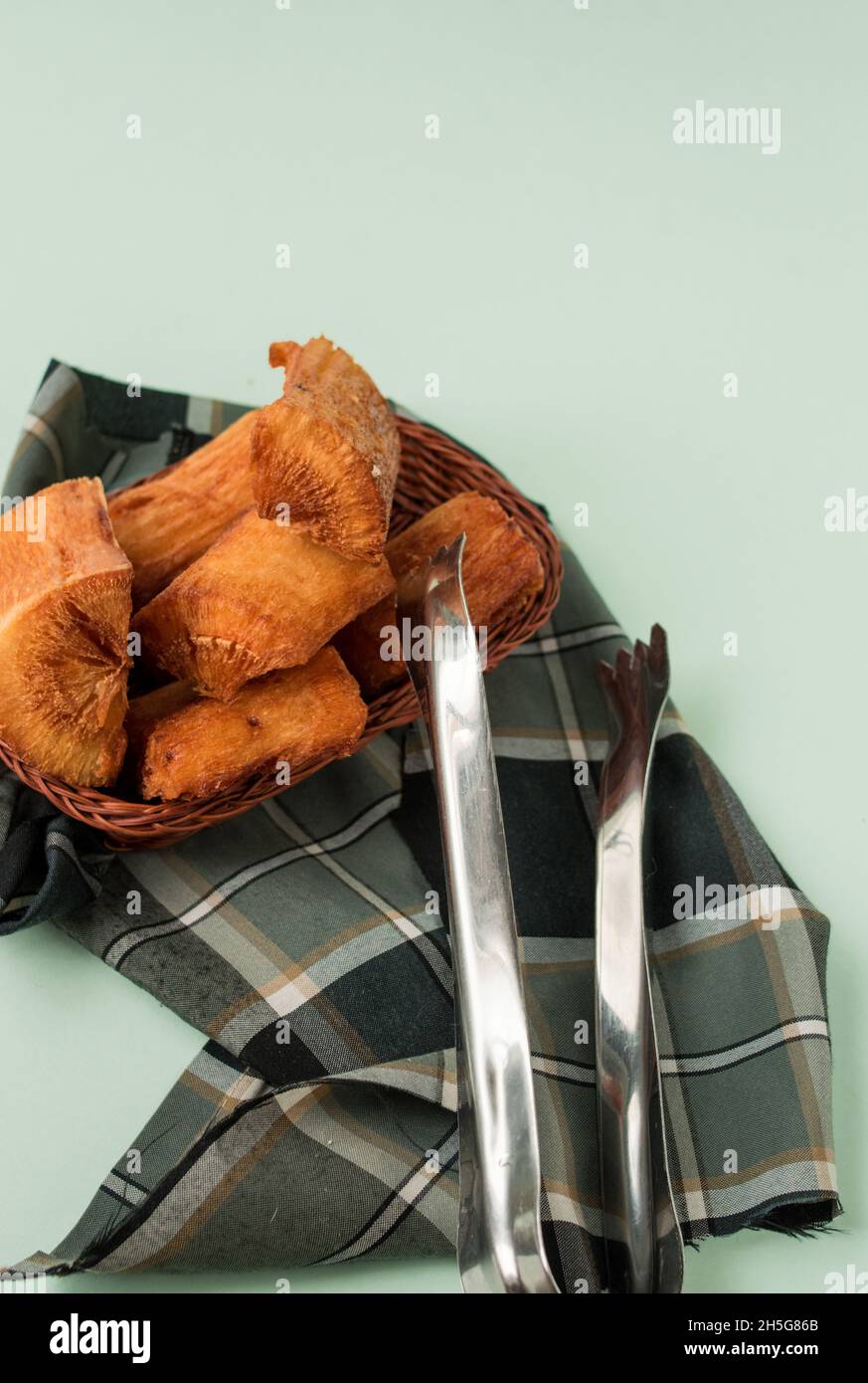 Fried yucca in a basket on a plaid piece of cloth on a green surface Stock Photo