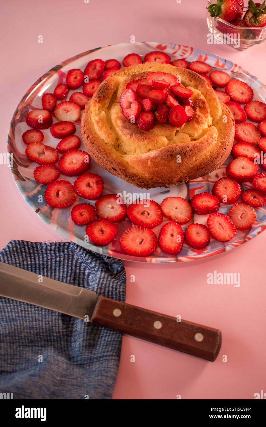 Strawberries, knife and cake with some strawberries on a pink background Stock Photo