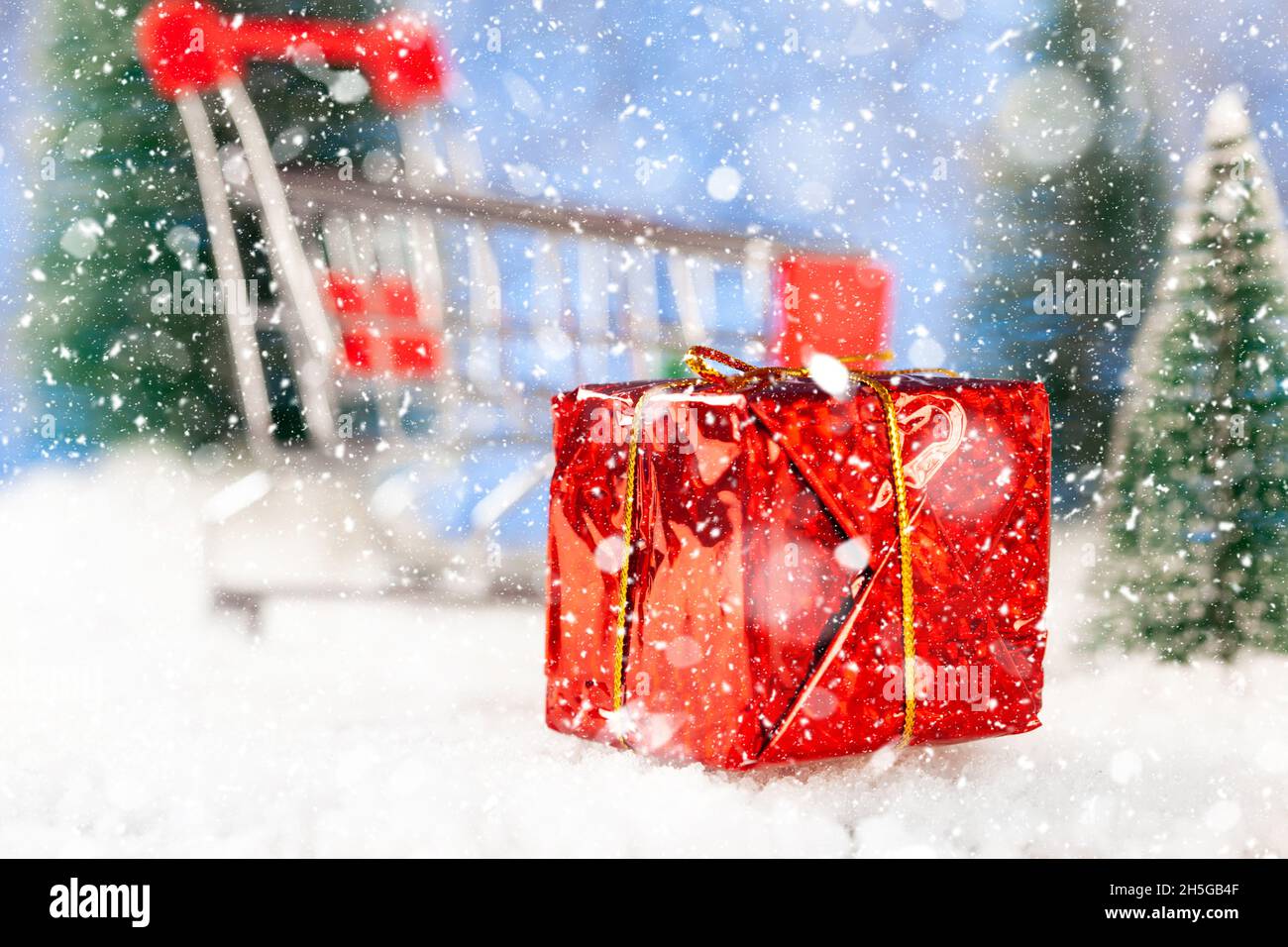 Christmas shopping. Red box with a gift on the background of a supermarket trolley. Around toy fir trees Stock Photo