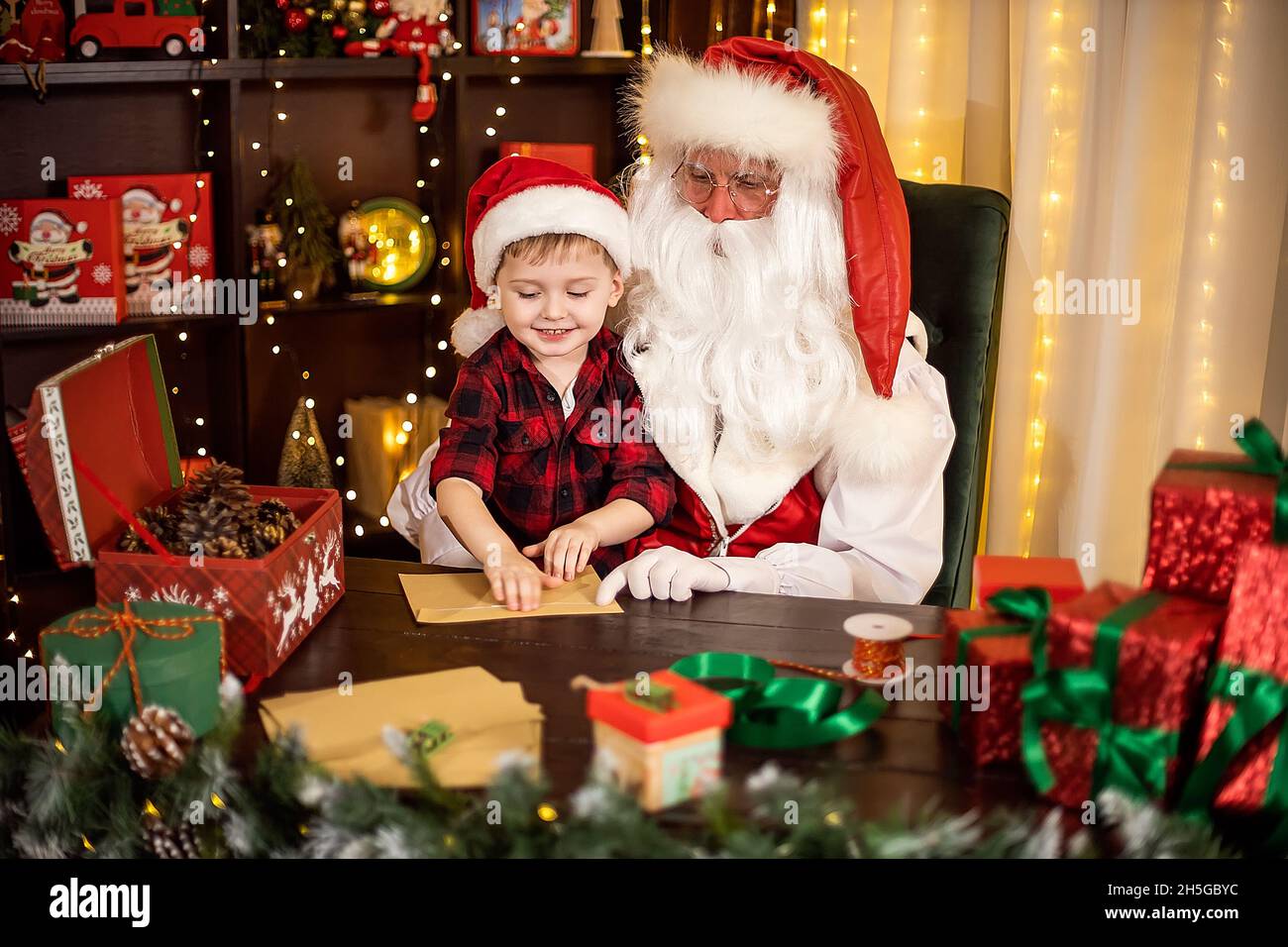 Little child boy visits Santa Claus helps him open envelopes with Christmas wishes. Holidays concept Stock Photo