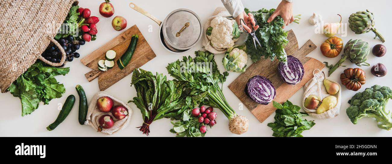 Female hands cutting greens over table with fresh seasonal vegetables Stock Photo