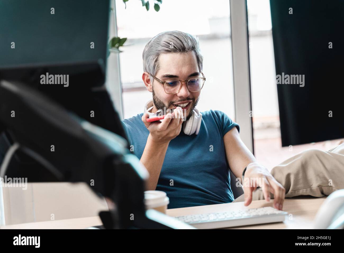 Happy millenial business man using mobile phone while working inside coworking office - Focus on face Stock Photo