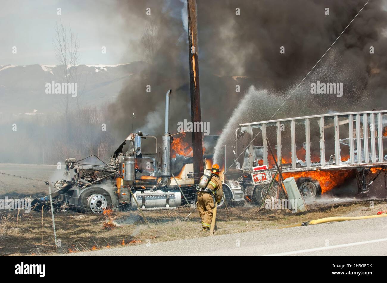 Firefighter hosing down a tractor-trailer truck on fire after an automobile accident; United States of America Stock Photo