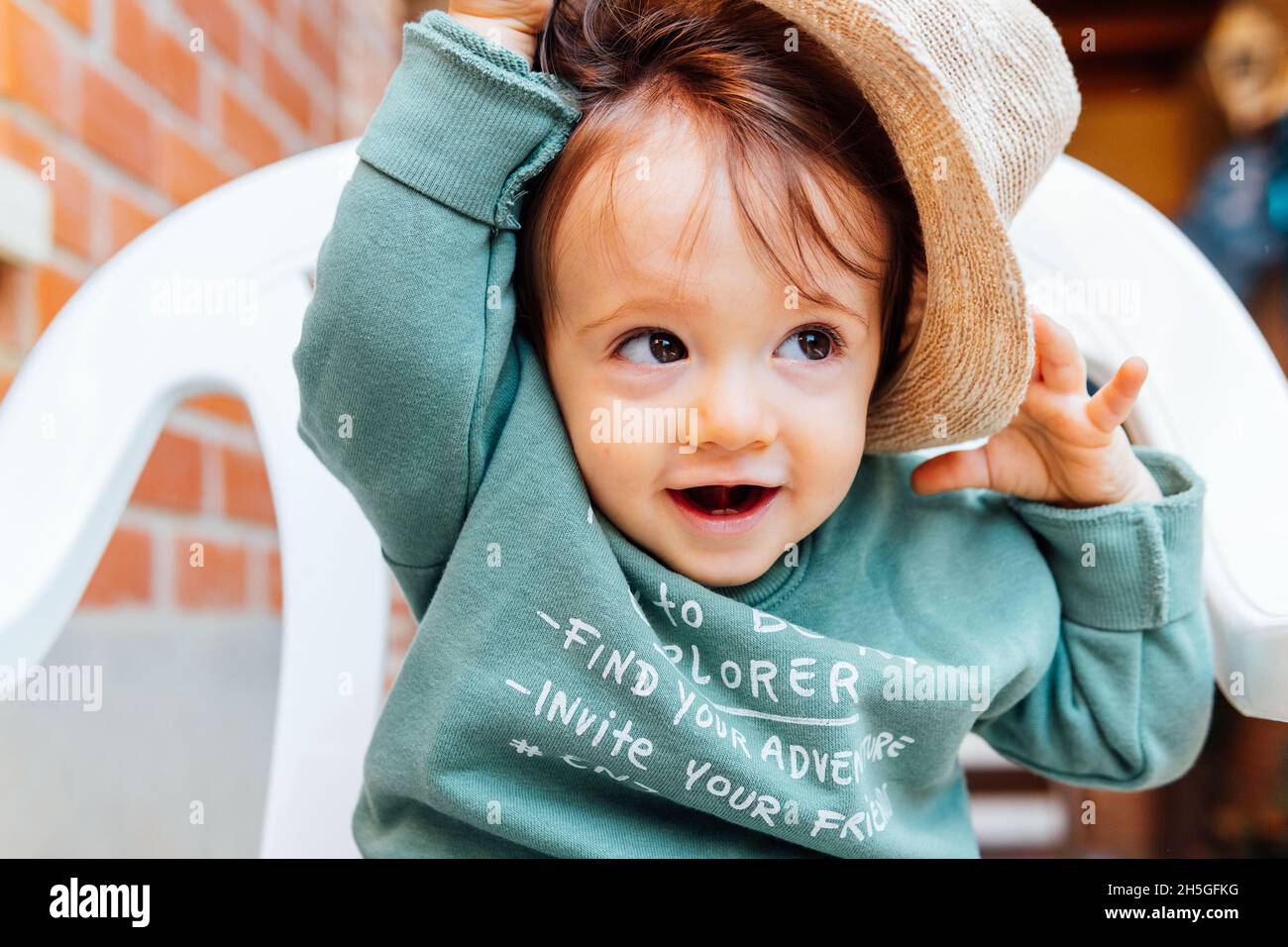lovely 1 year old boy sitting on a chair putting on a hat Stock Photo Alamy