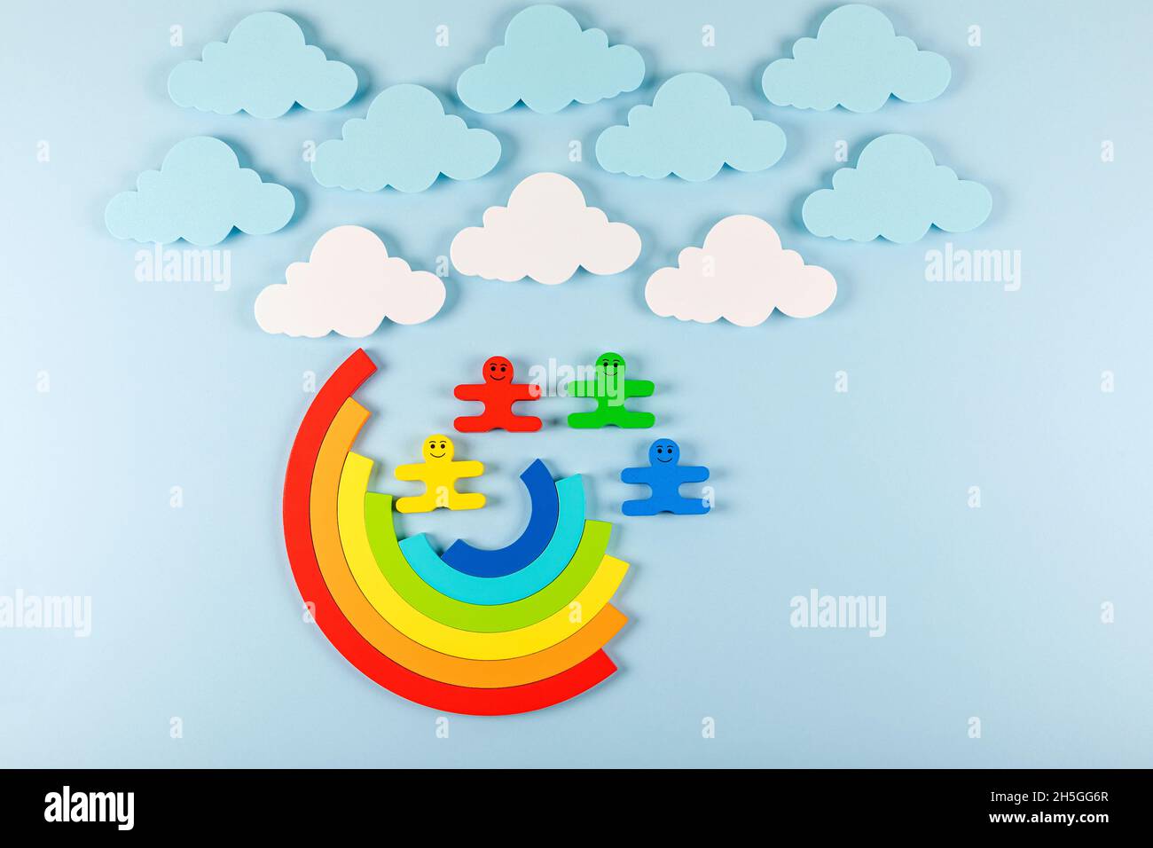 International Children's Day concept. Wooden toy children with rainbow on the bright blue background. Flat lay. Copy space. Stock Photo