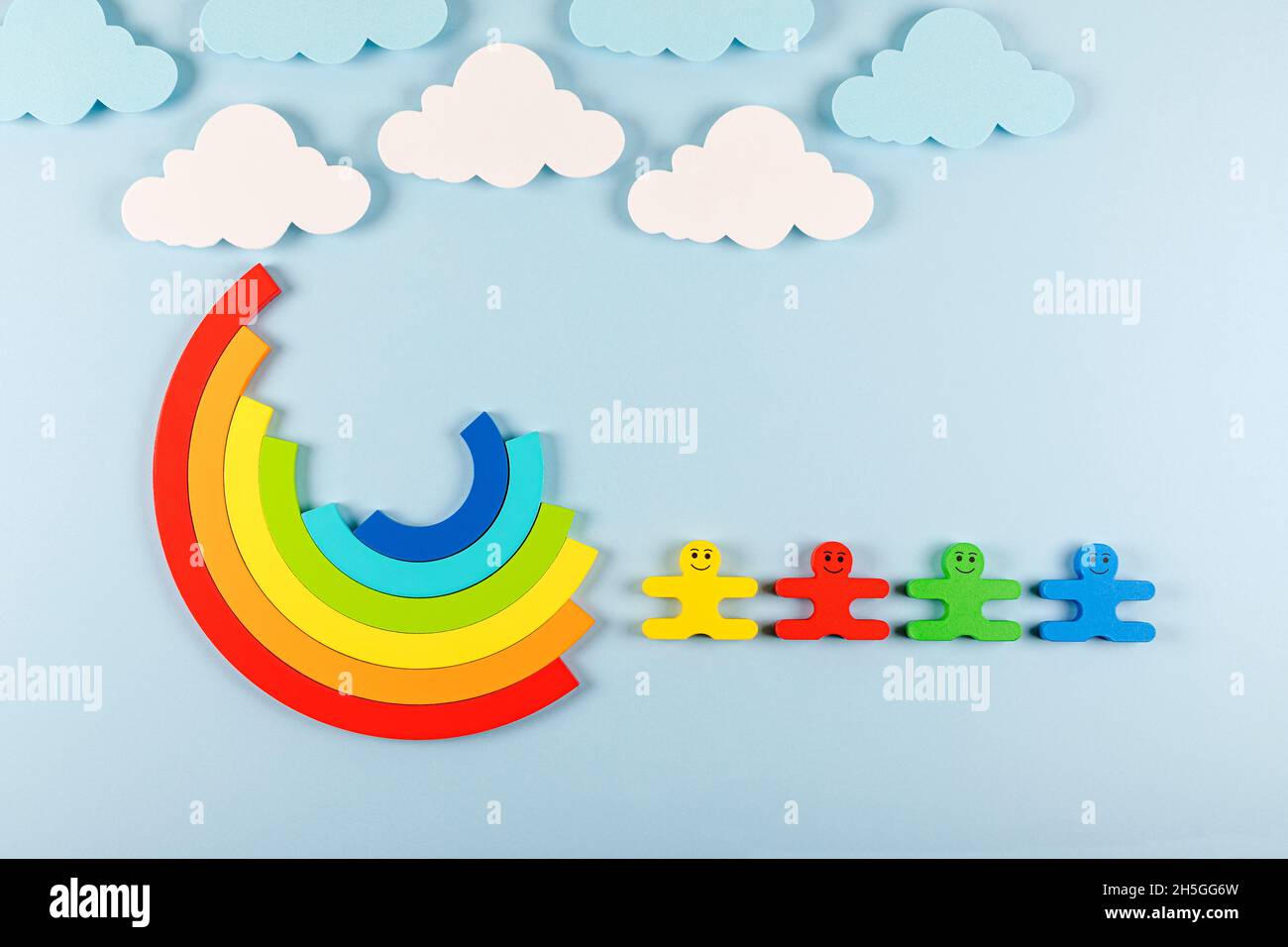 International Children's Day concept. Wooden toy children with rainbow on the bright blue background. Flat lay. Copy space. Stock Photo