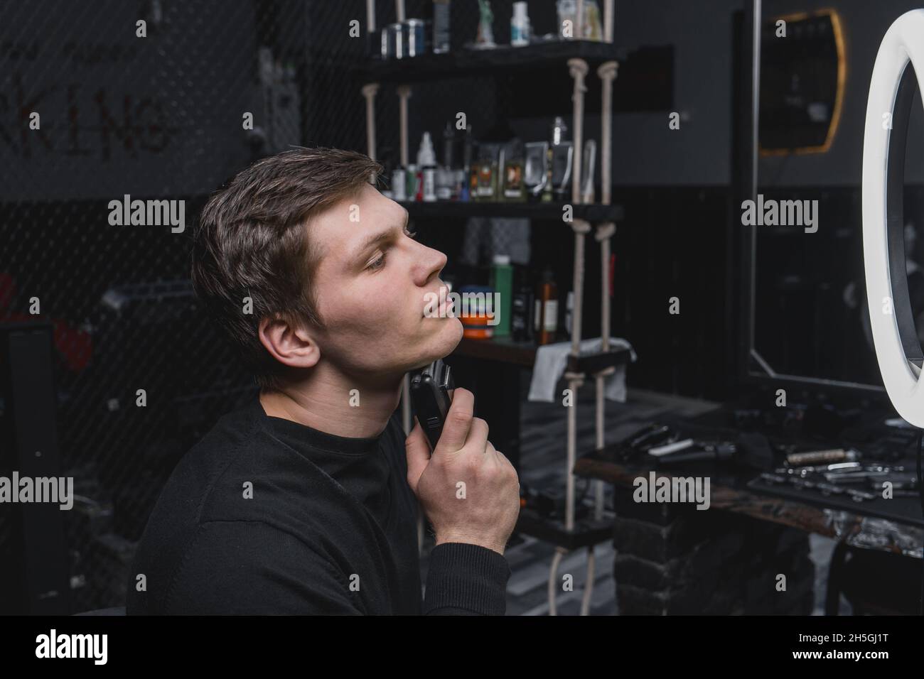 A serious young guy of Caucasian appearance with dark hair shaves with ...