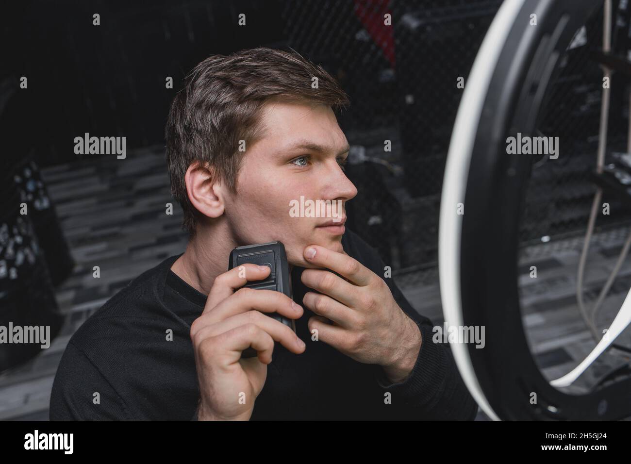 A serious young guy of Caucasian appearance with dark hair shaves with ...