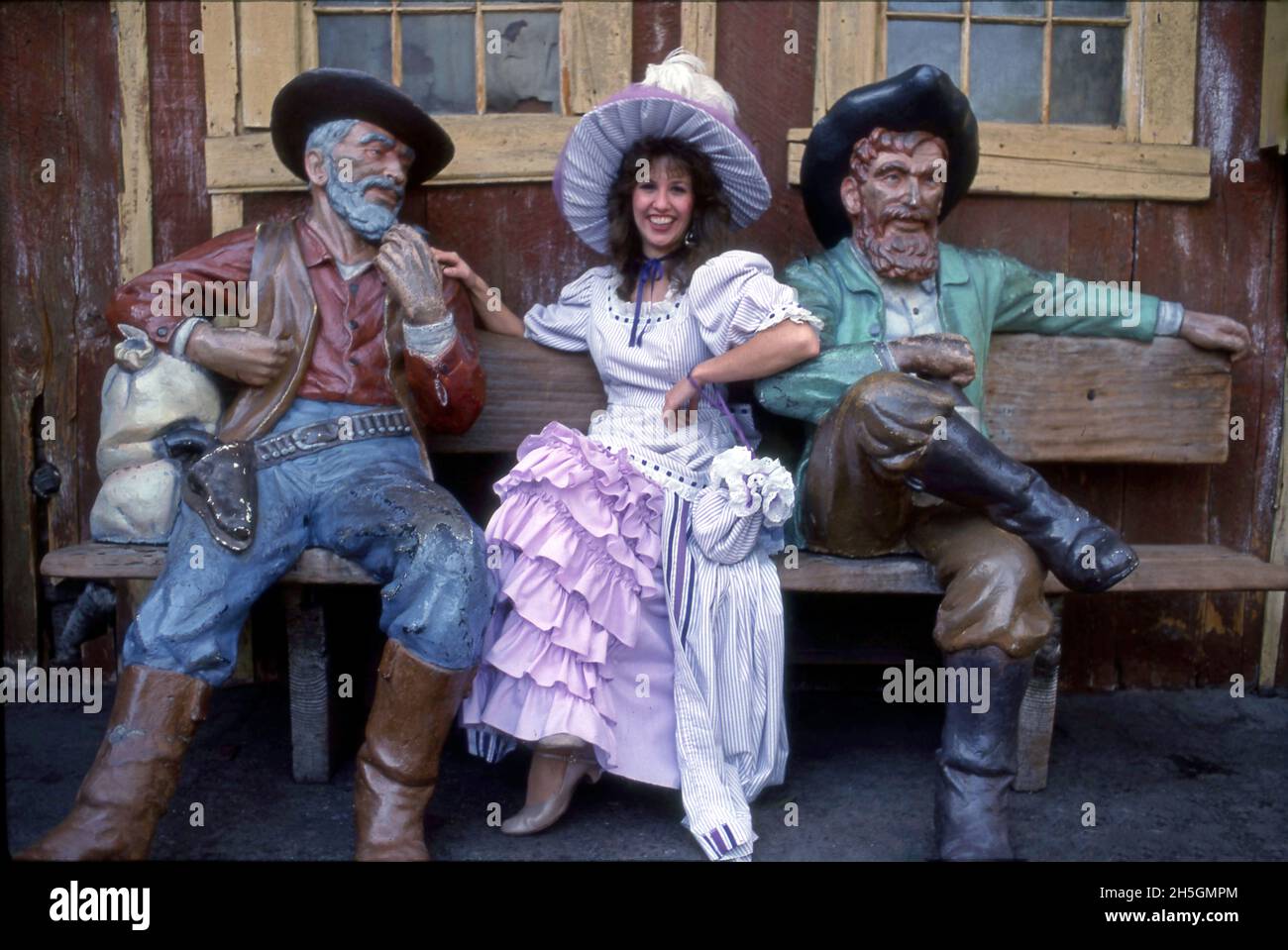 Woman in period costume posing with wood carved figures of men from the Wild West period at Knott's amusement park in Buena Park, CA Stock Photo