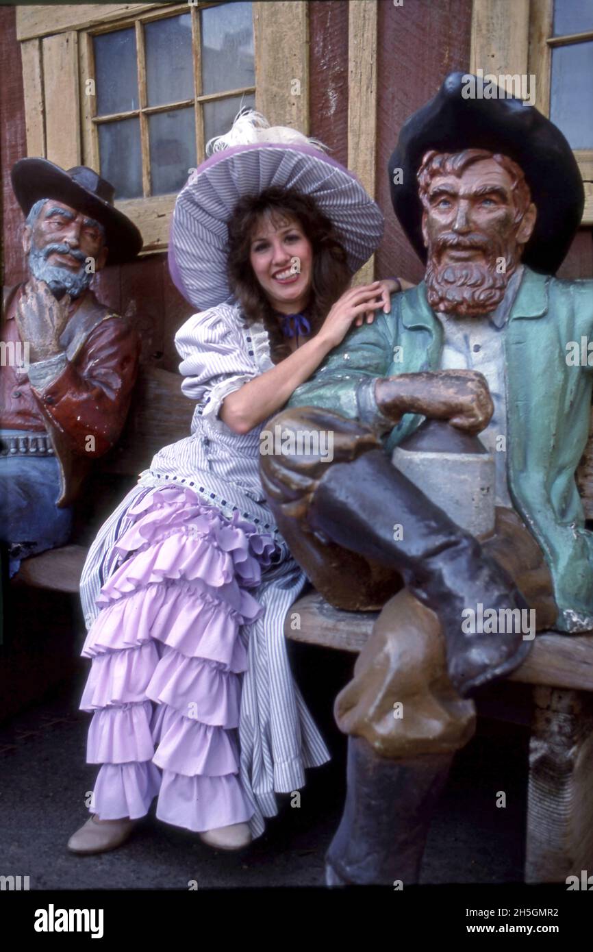 Woman in period costume posing with wood carved figures of men from the Wild West period at Knott's amusement park in Buena Park, CA Stock Photo