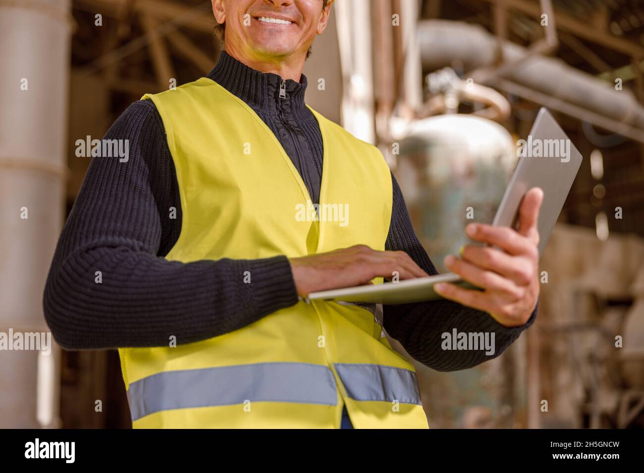 Joyful male worker using notebook at factory Stock Photo