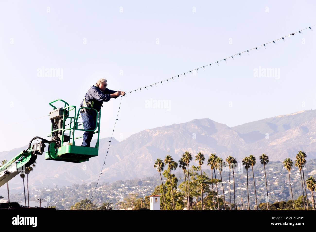 Worker on a lift installing a string of Christmas lights Stock Photo
