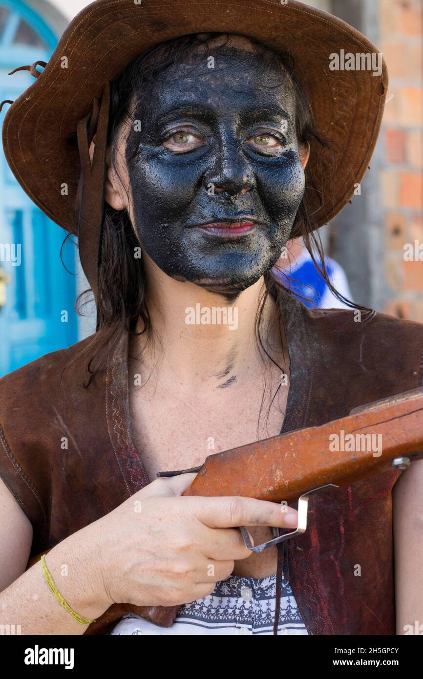 Caucasian woman with face made up in black color. She is wearing a pink hat and holding a brown colored gun. Acupe, Bahia, Brazil. Stock Photo