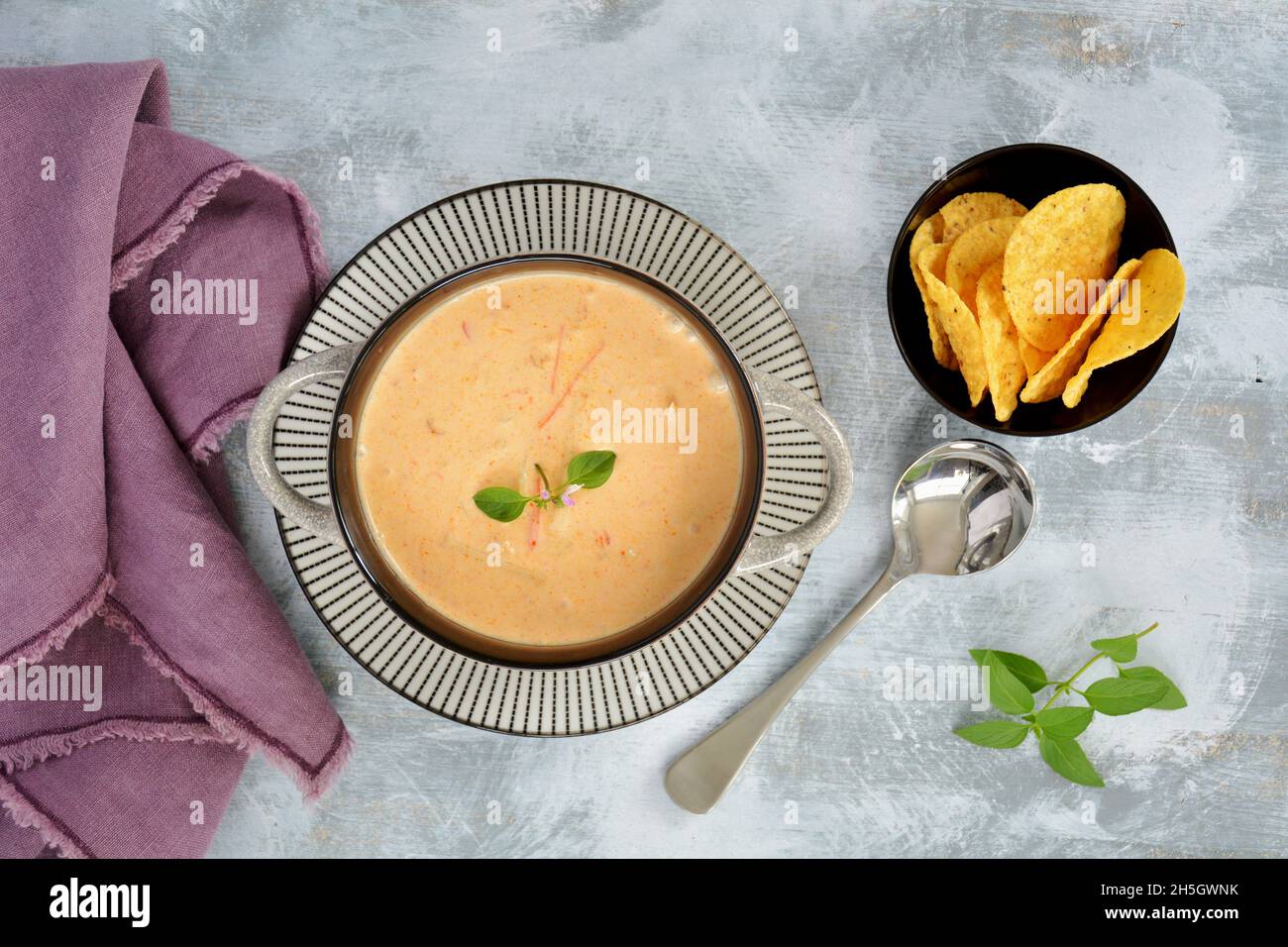 Spicy Thai red curry and coconut soup in rustic earthenware bowl with crackers in horizontal format.Thai basil garnish. Stock Photo