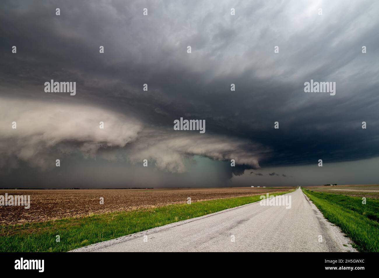 Dangerous storm with shelf cloud approaches quickly over a farm field along a country road. Stock Photo