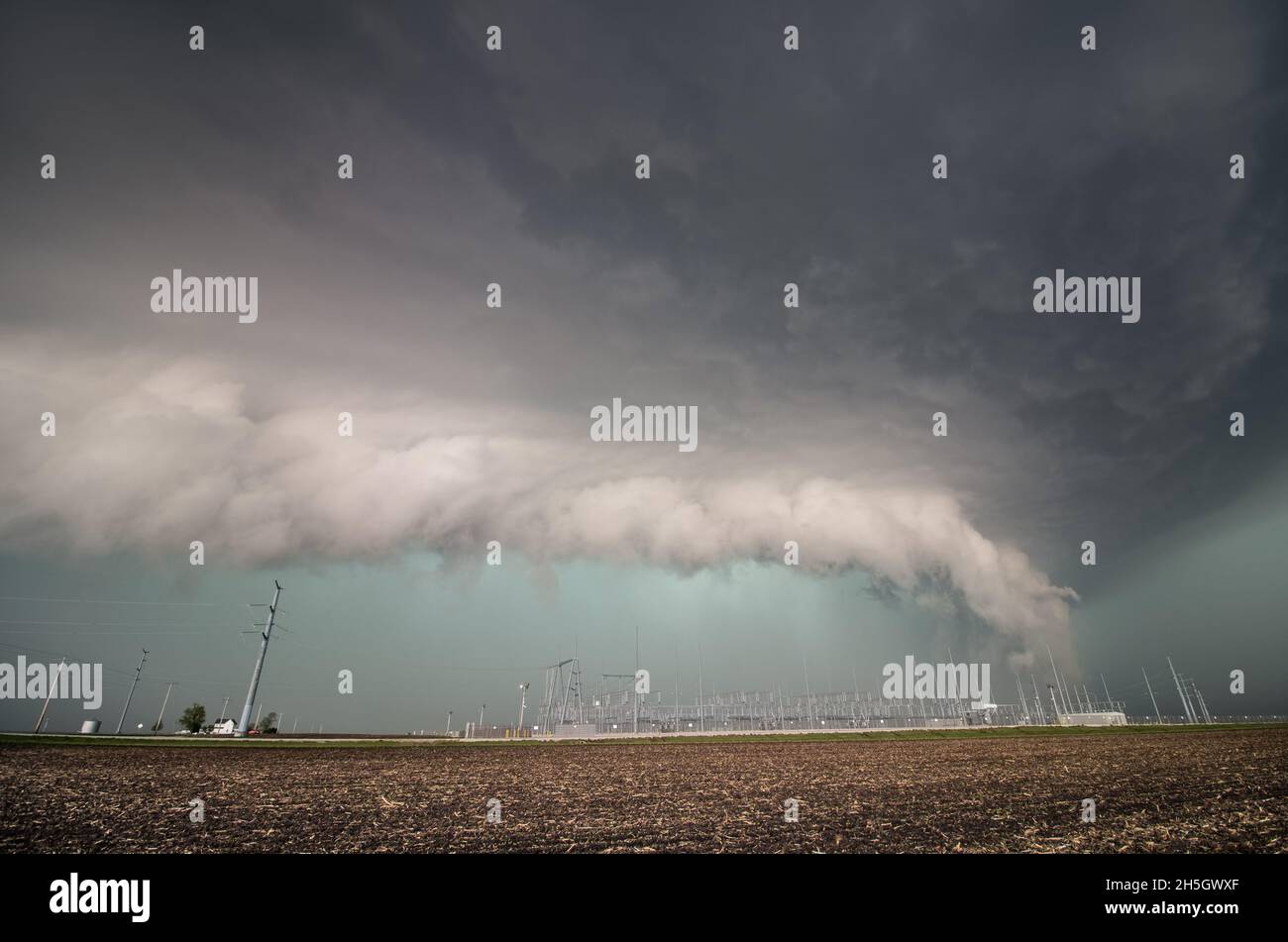A severe thunderstorm and low shelf cloud loom over electrical equipment and power poles. Stock Photo
