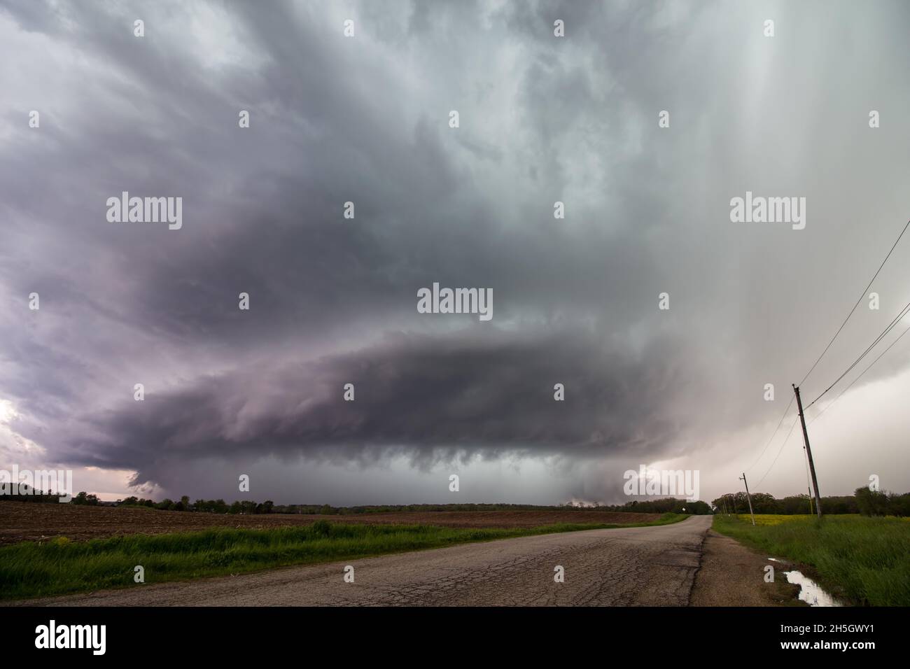 Looking down a road at a supercell storm as it approaches over a farm field. Stock Photo