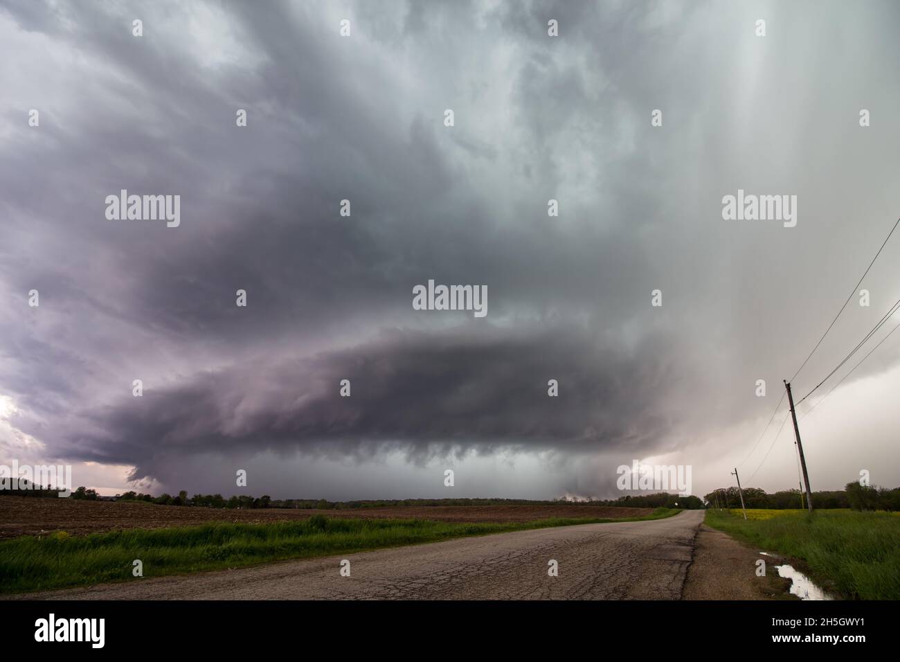 Looking down a road at a supercell storm as it approaches over a farm ...