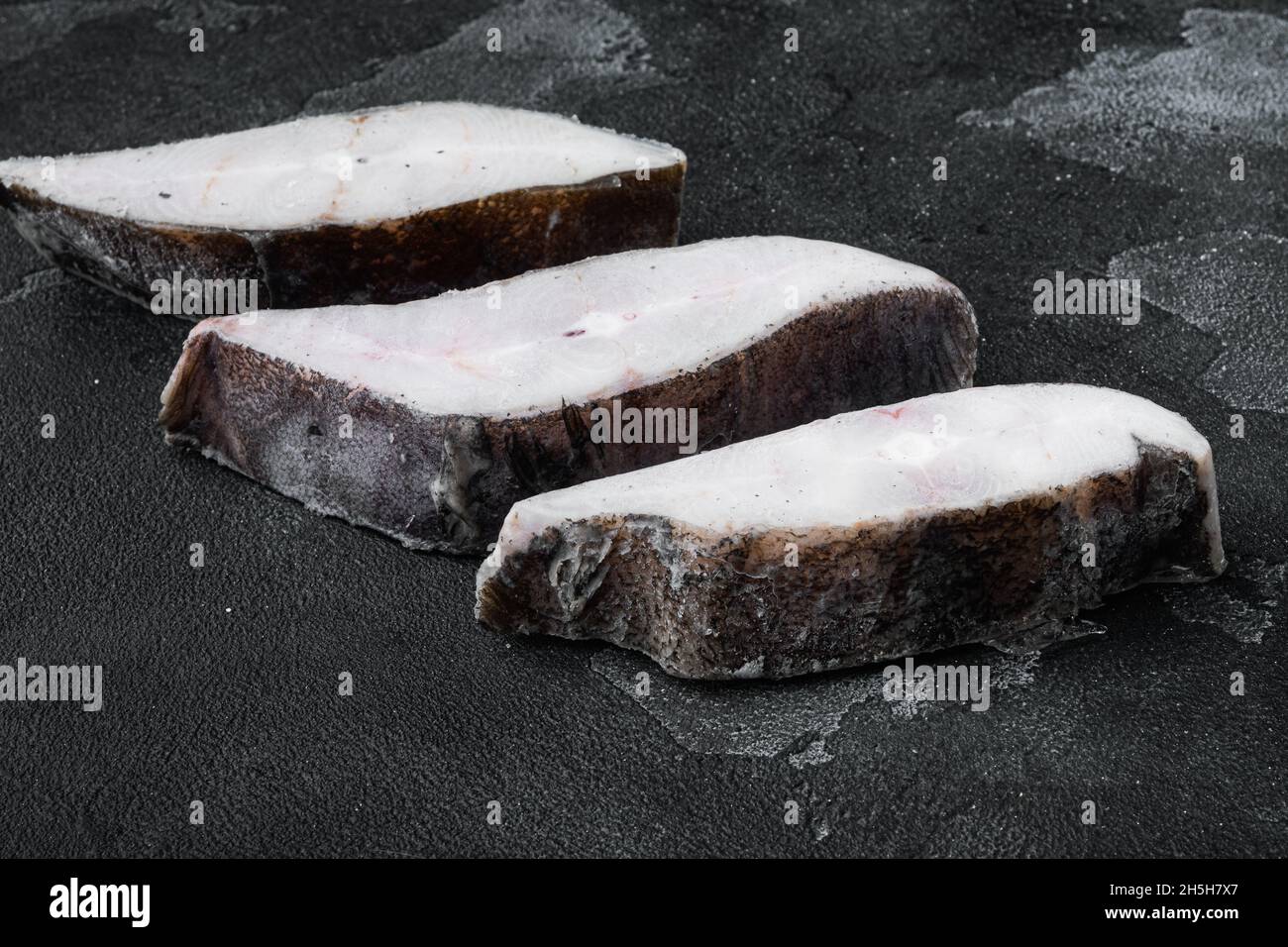 Frozen halibut steak set, on black dark stone table background Stock