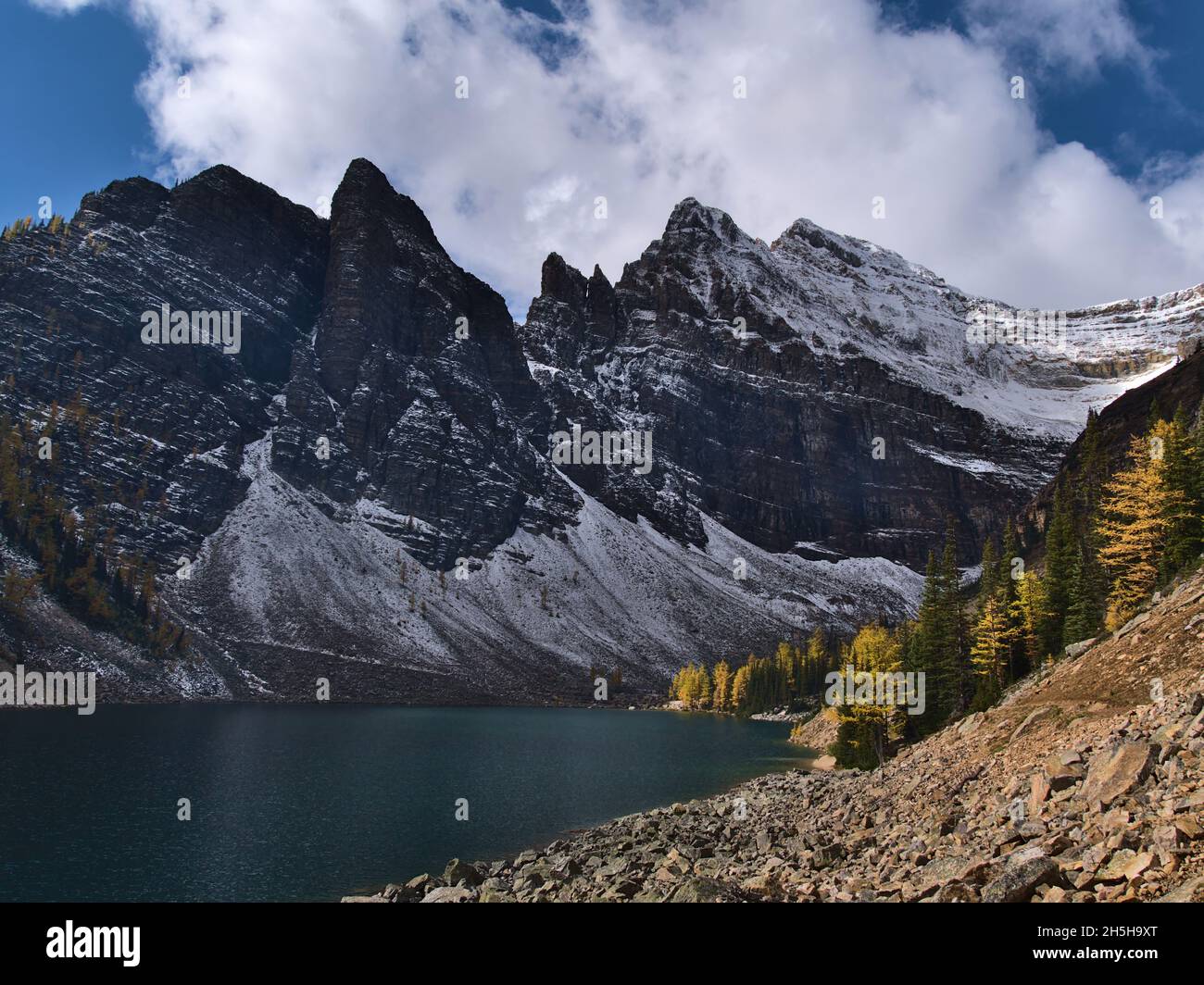 View of Lake Agnes in autumn with larch trees on the shore and snow-covered rock face of Mount Whyte near Lake Louise, Banff National Park, Canada. Stock Photo