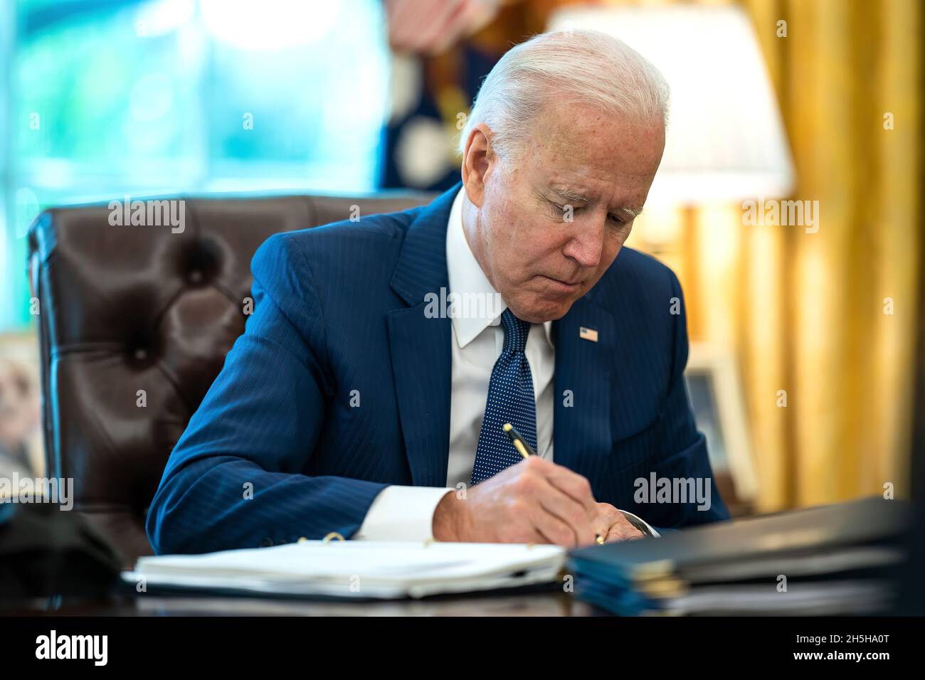 President Joe Biden makes notes during a meeting with White House staff ...