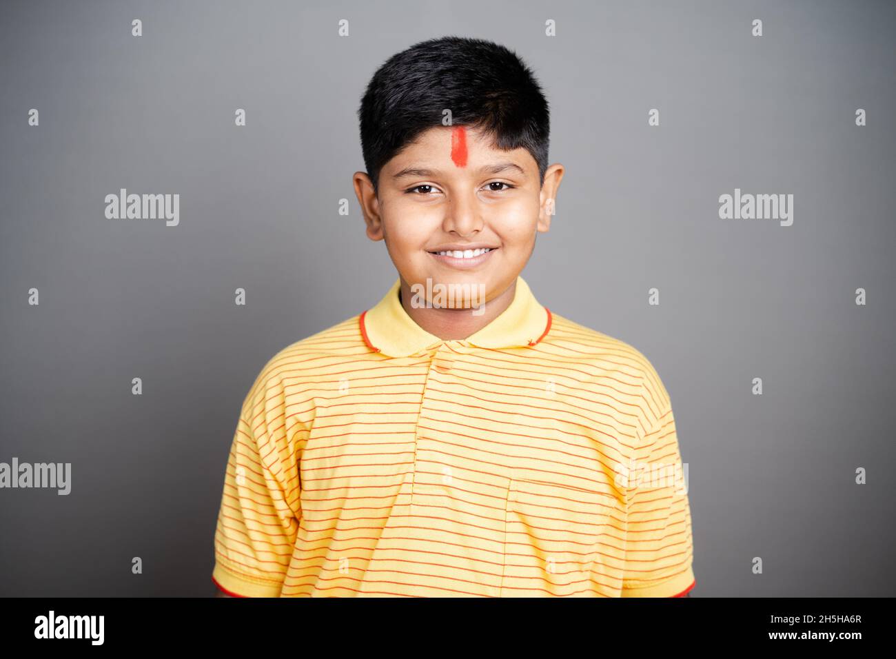 Happy Hindu kid with kumkum Bindi or Tilak on forehead by looking at camera on studio background - concept of smiling and positive joyful expression Stock Photo